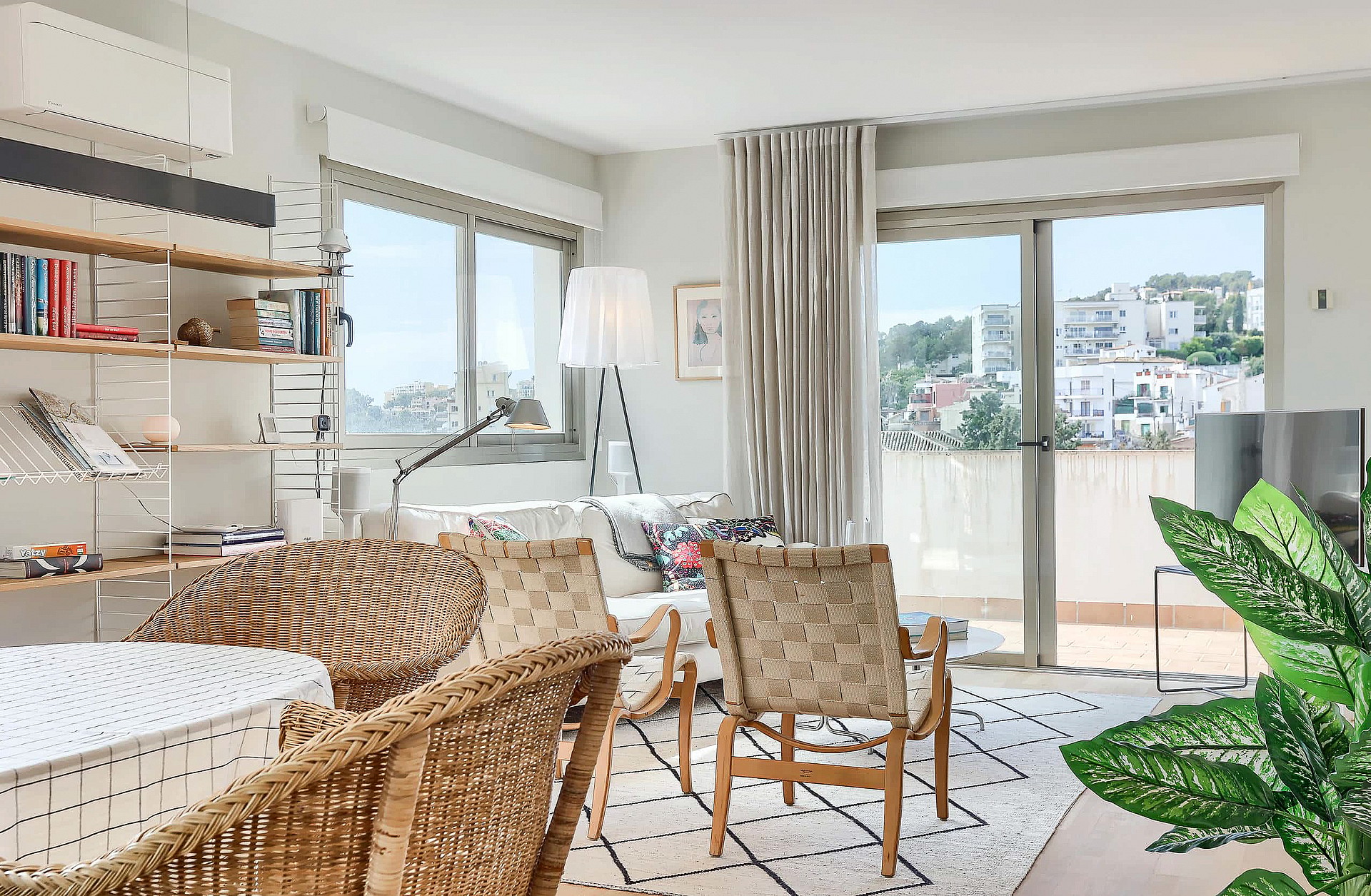 Bright living room featuring rattan armchairs, a patterned area rug, and floor-to-ceiling glass doors opening to a balcony.