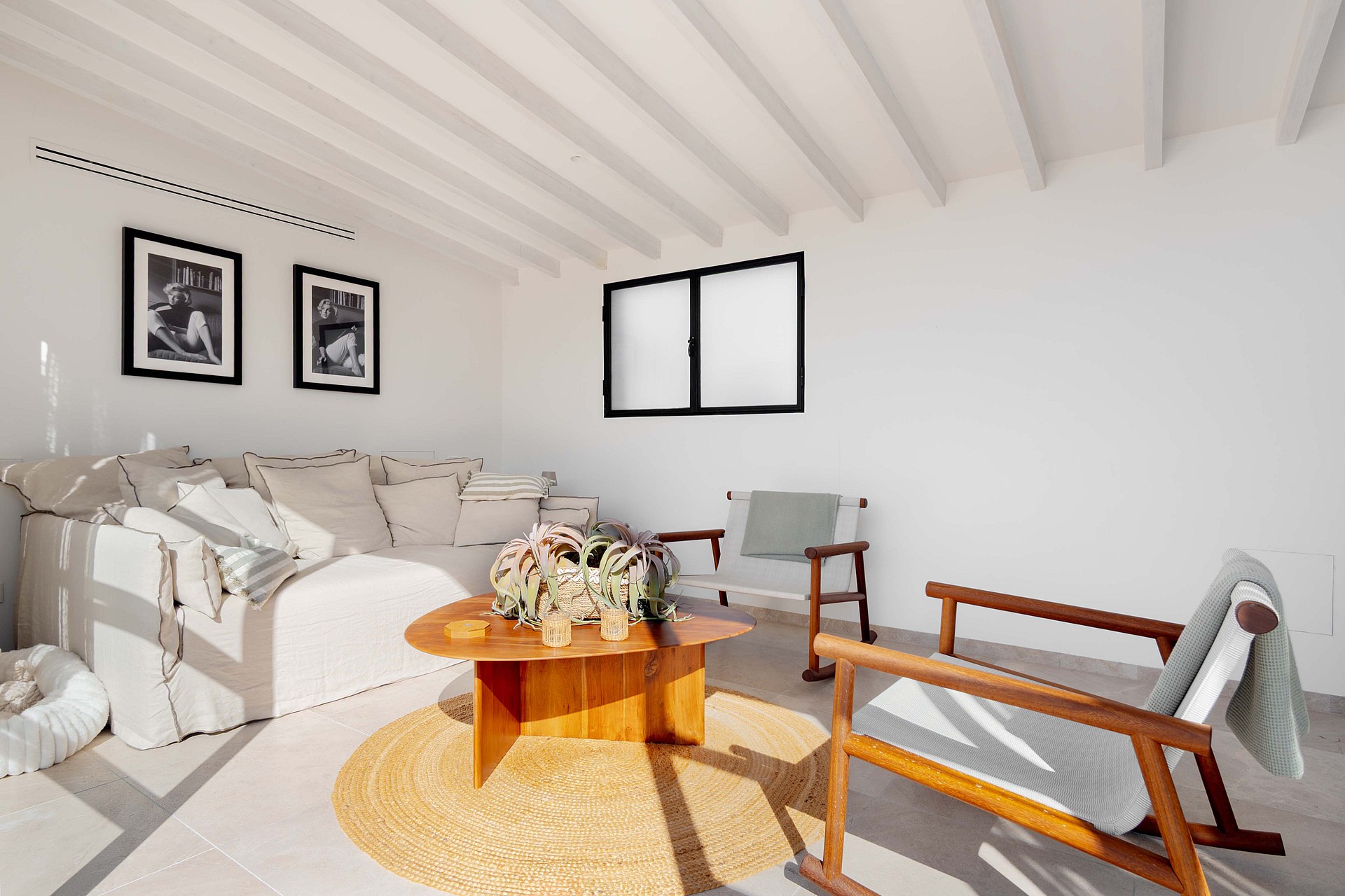 Interior view of a living space with white walls, exposed white ceiling beams, a light-colored sofa, and a wooden coffee table.