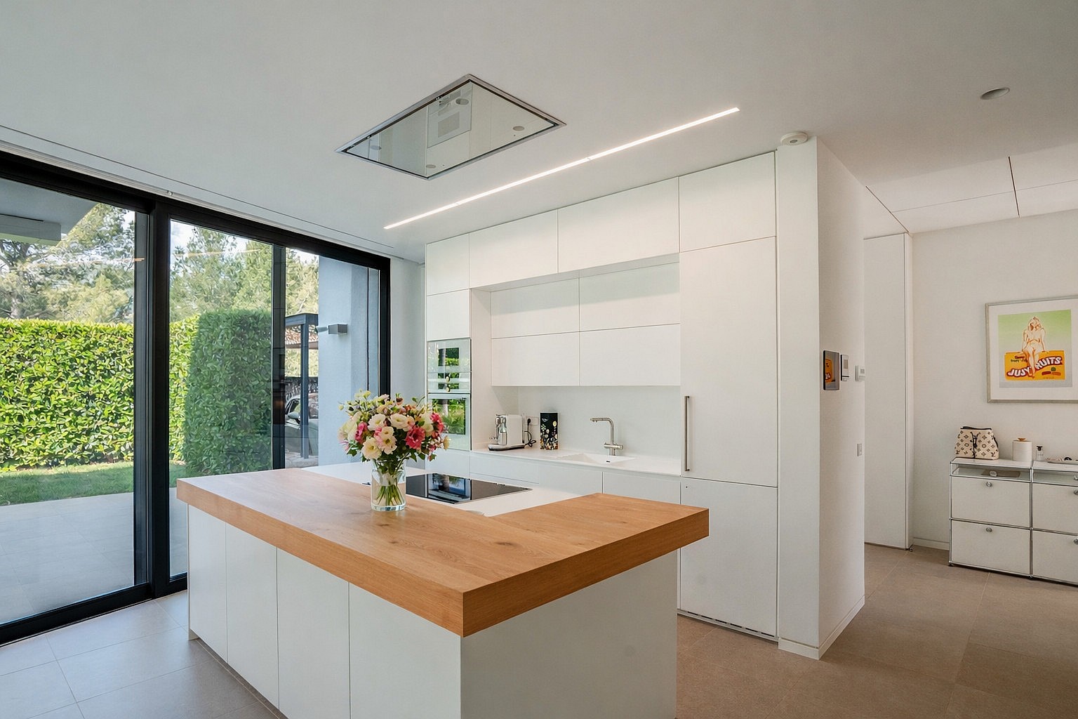 White handleless kitchen with oak-topped island, induction hob and floor-to-ceiling sliding doors to the garden.
