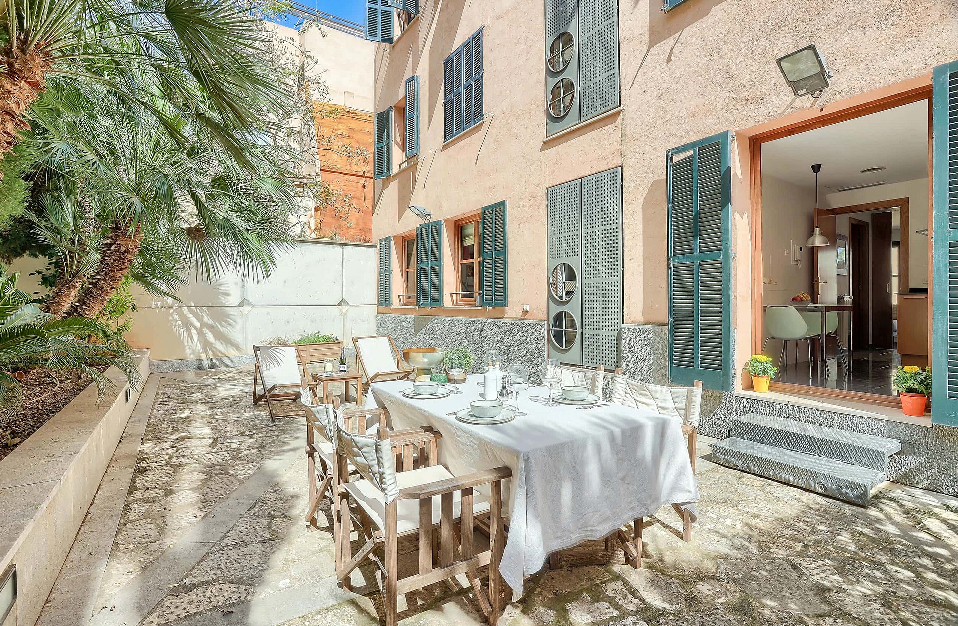 Outdoor terrace in a historic Old Town building with a dining table, folding wooden chairs, and green shutters.