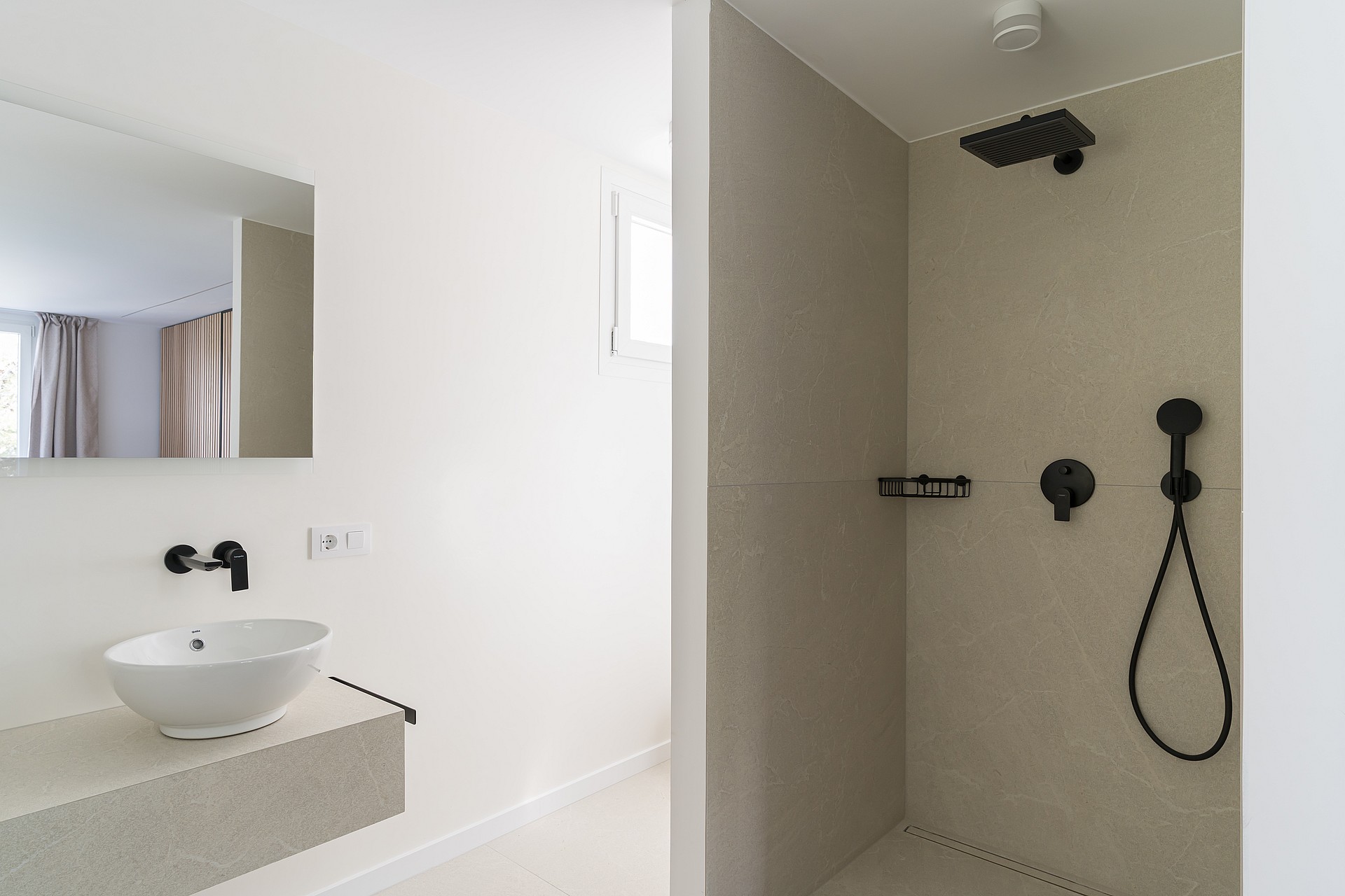 Modern walk-in shower featuring large-format sand-colored tiles and contrasting matte black rain shower and handheld spray.