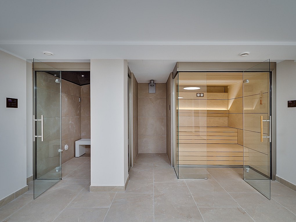 Spa moderno con sauna de madera y baño turco con revestimiento de piedra e iluminación integrada.