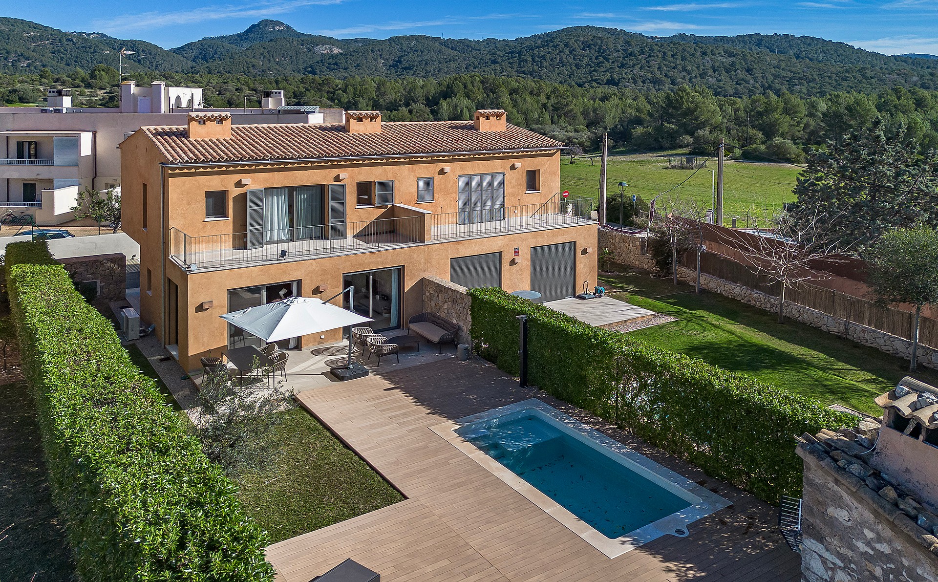 Aerial view of a Mediterranean townhouse with a terracotta roof, private pool, and landscaped garden against a mountain backdrop.