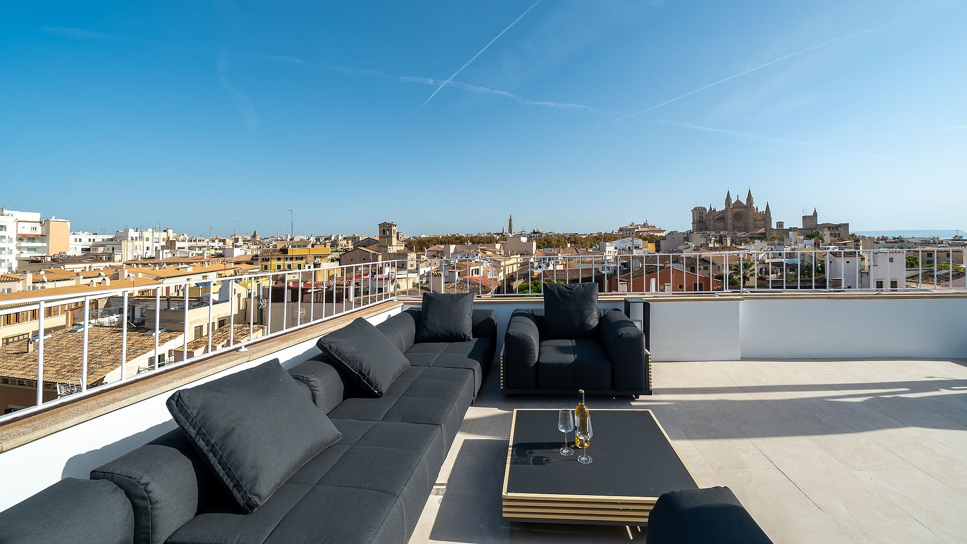 Modern black lounge furniture on a sun-drenched rooftop terrace overlooking Palma Old Town and the Cathedral.