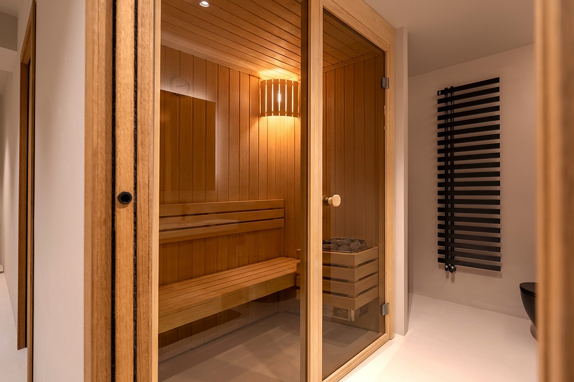 Interior view of a modern sauna featuring light wood paneling, slatted benches, and a glass entry door.