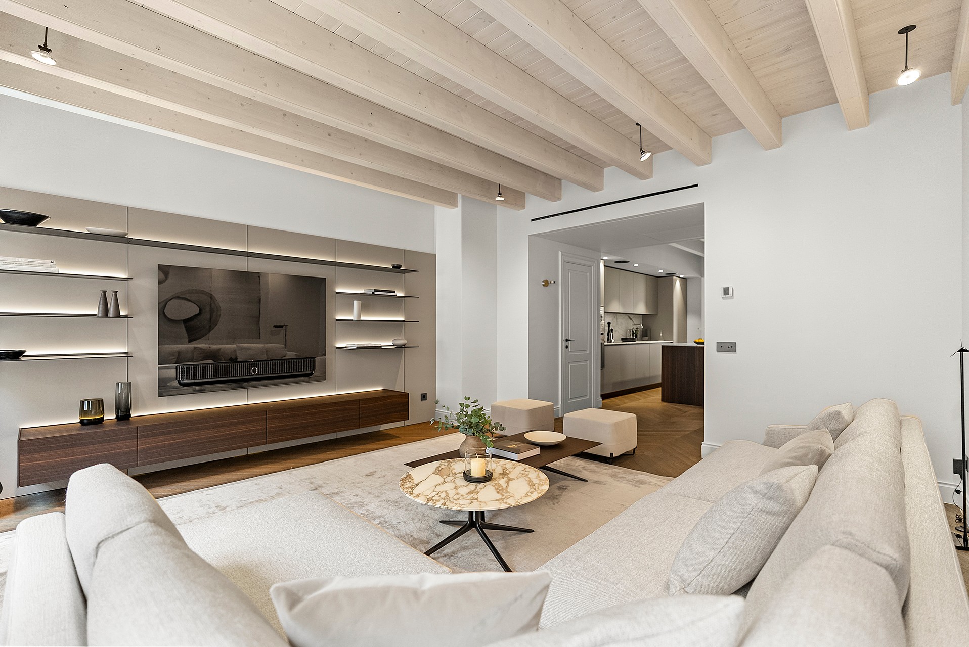 Contemporary living room featuring whitewashed ceiling beams, integrated backlit shelving, and a marble coffee table.