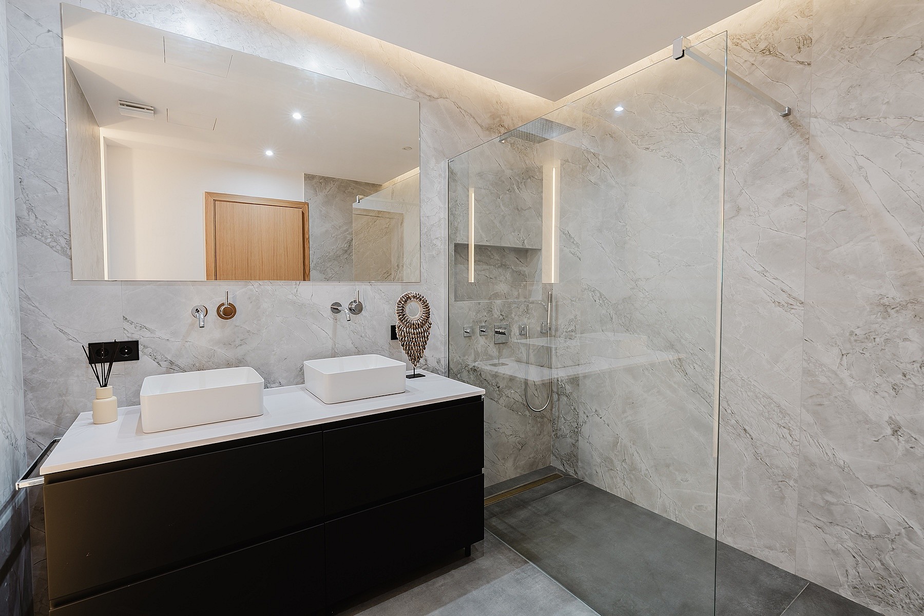 A modern bathroom featuring a dark vanity with two white vessel sinks, a wall-to-wall mirror, and a walk-in glass shower.