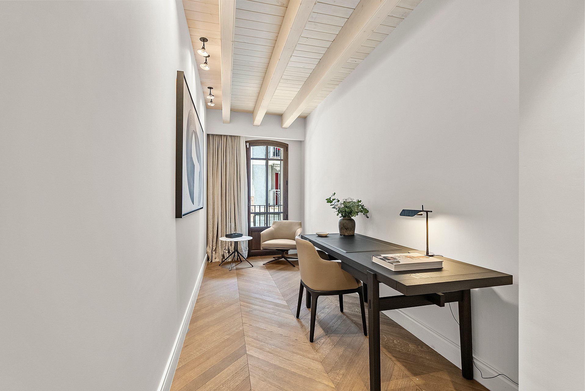 Minimalist home office featuring chevron wood flooring, exposed timber beams, a dark desk, and an arched glass door.
