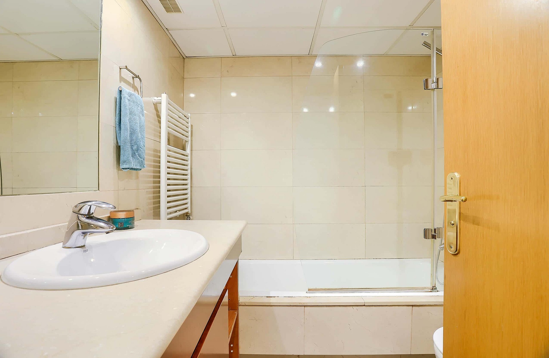 Bathroom interior featuring a white vanity with oval basin, wall mirror, towel rack, and a bathtub with a tiled enclosure.