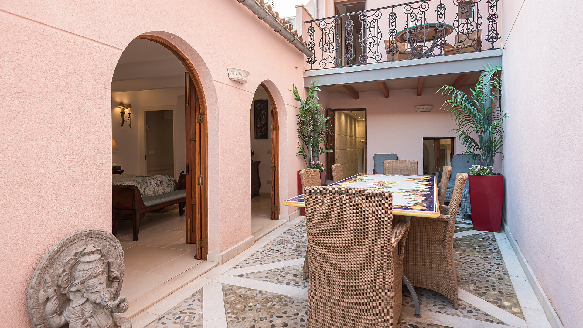 Pink-walled courtyard patio with a tiled dining table, potted plants and arched doorways