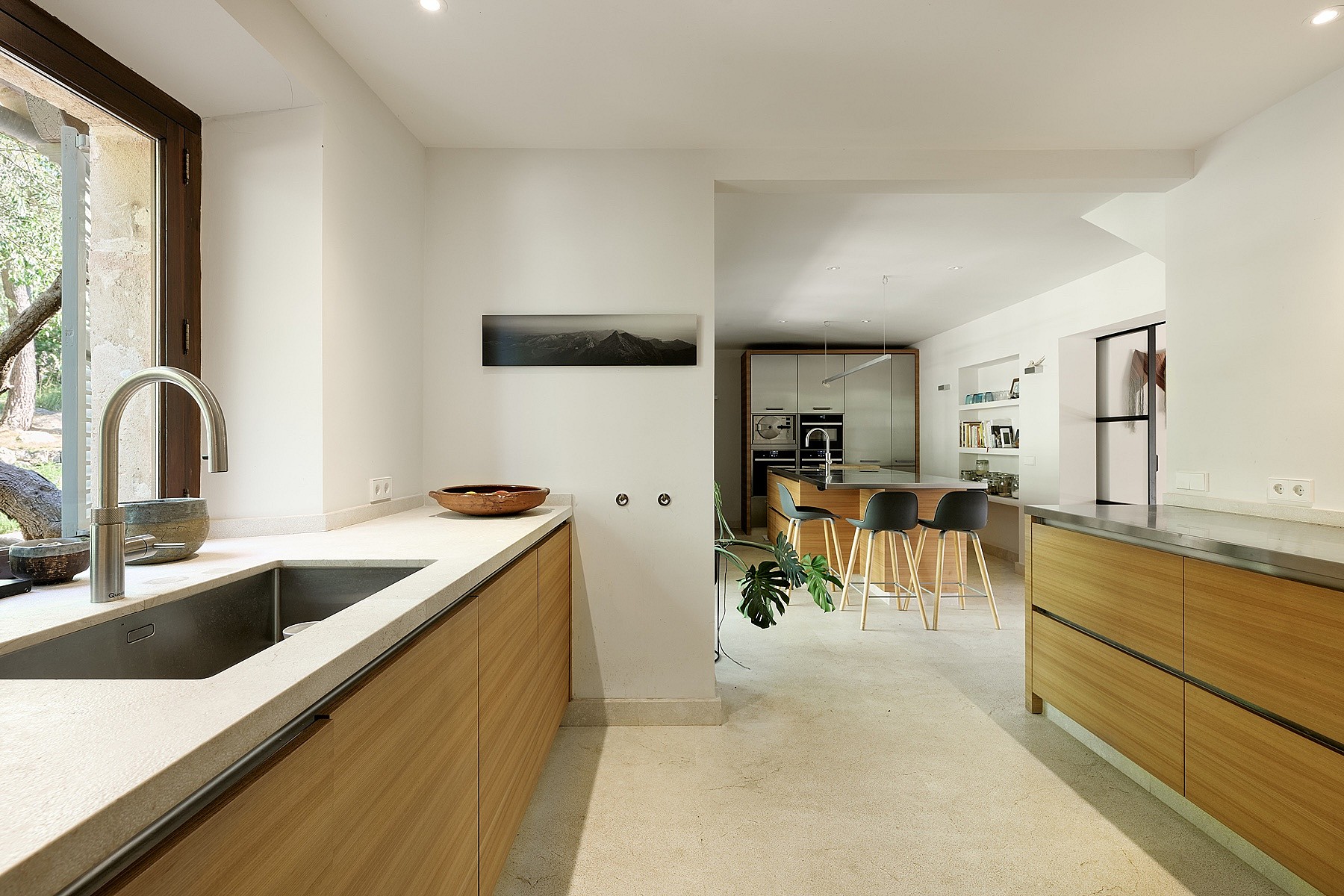 Modern kitchen interior featuring horizontal grain oak cabinets, light stone countertops, and a stainless steel sink.