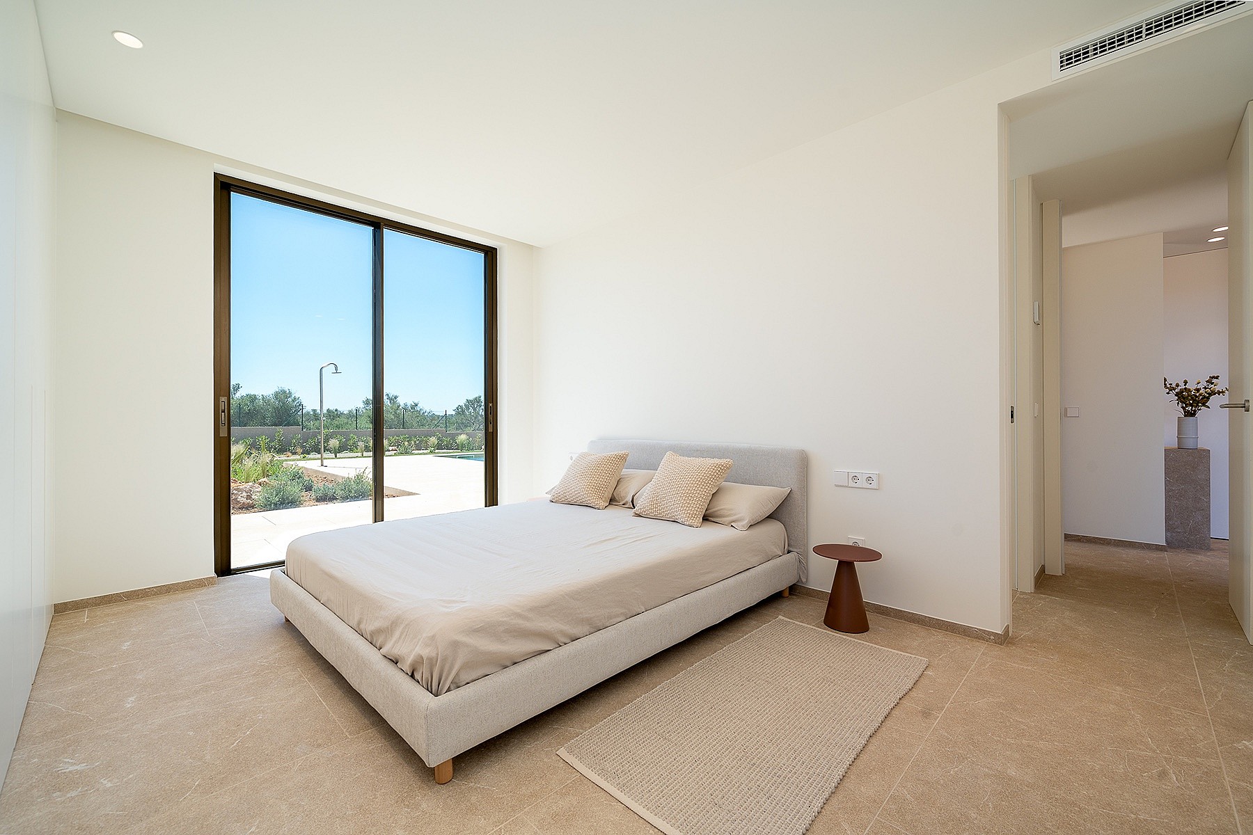Minimalist bedroom with neutral linens, a natural fiber rug, and floor-to-ceiling sliding glass doors opening to a garden.