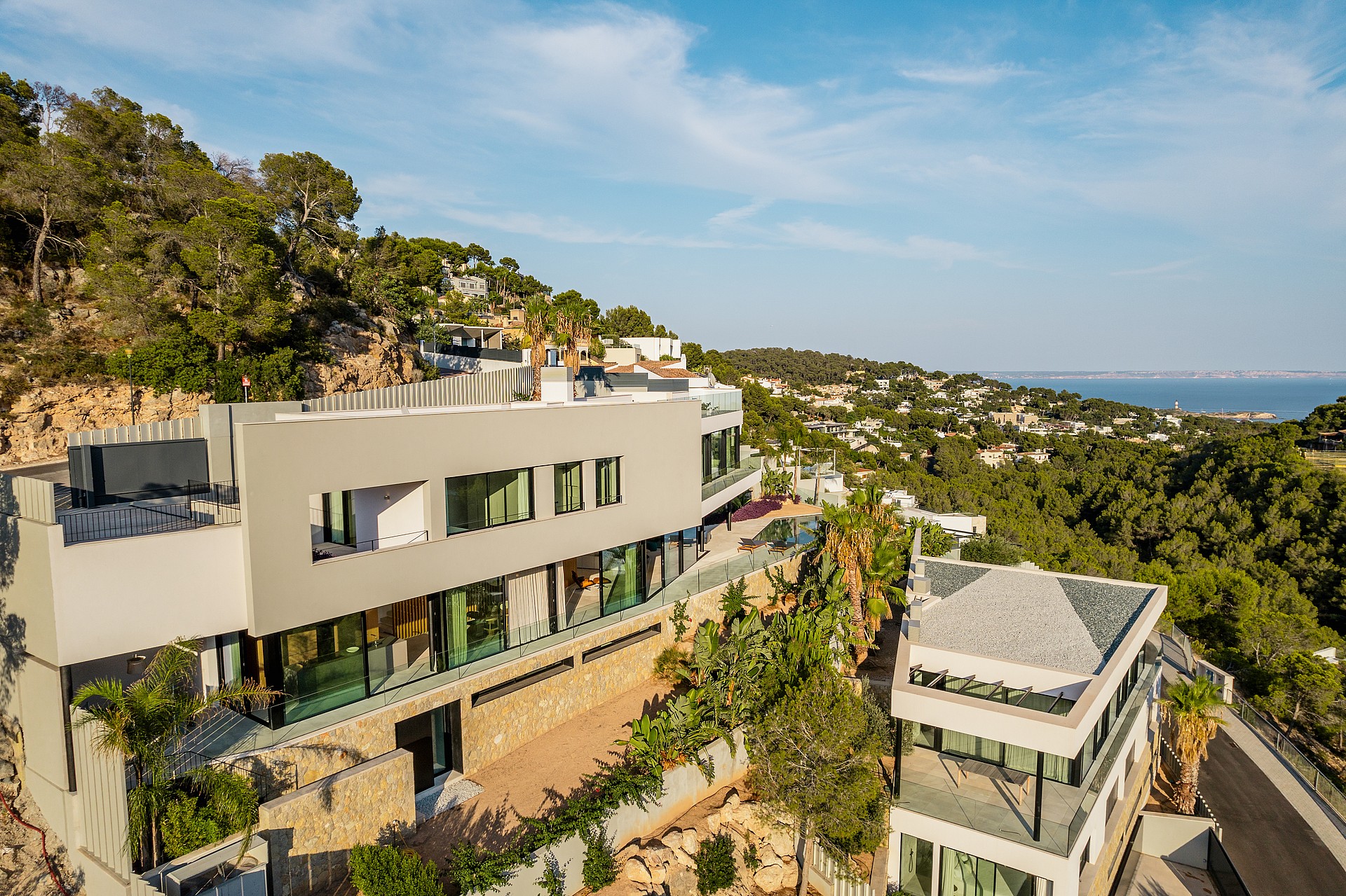Aerial view of a contemporary multi-level villa with stone retaining walls and glass facade set into a hillside.