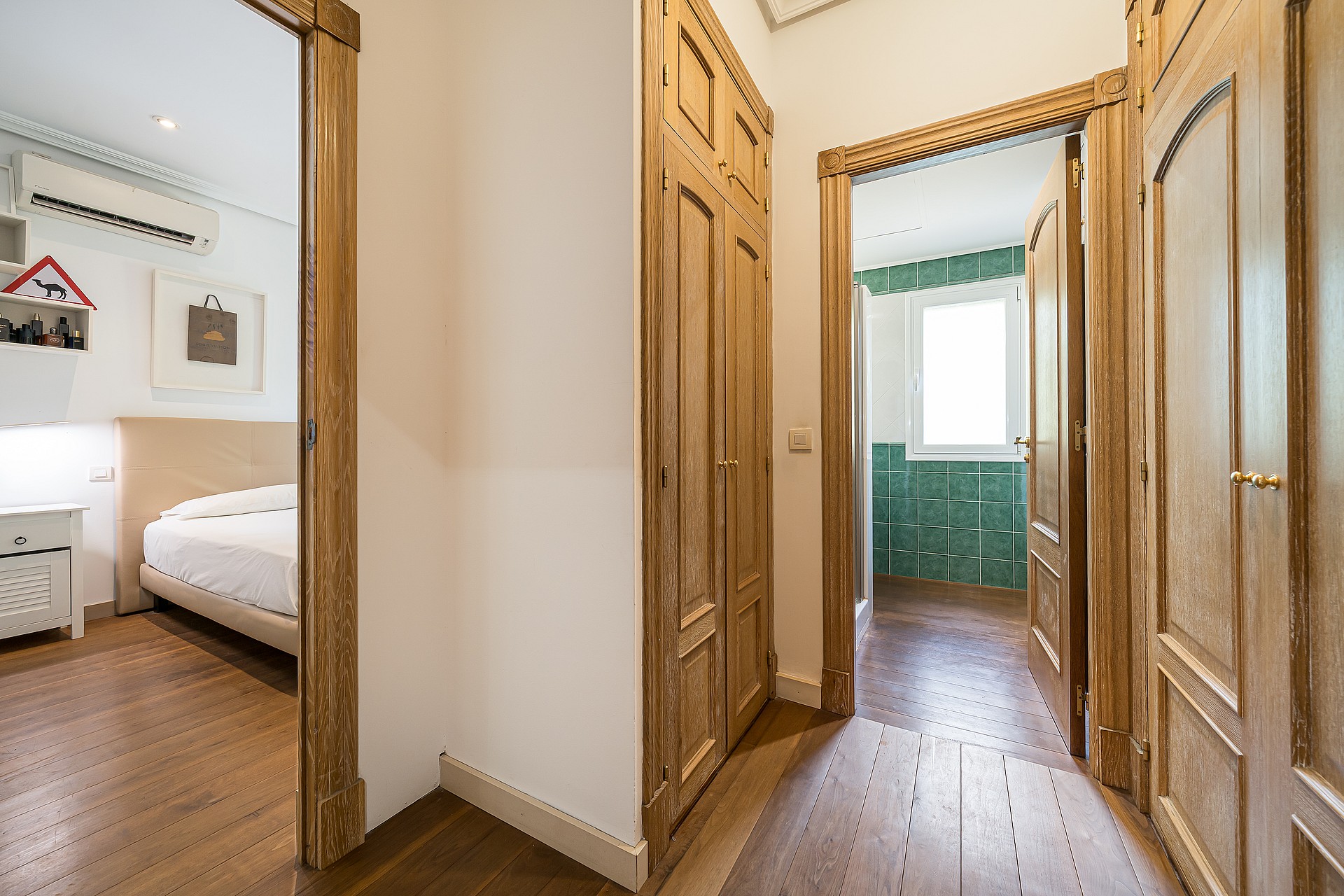 A corridor in a villa featuring natural wood built-in wardrobes and doorways leading into two bedrooms with wooden flooring.