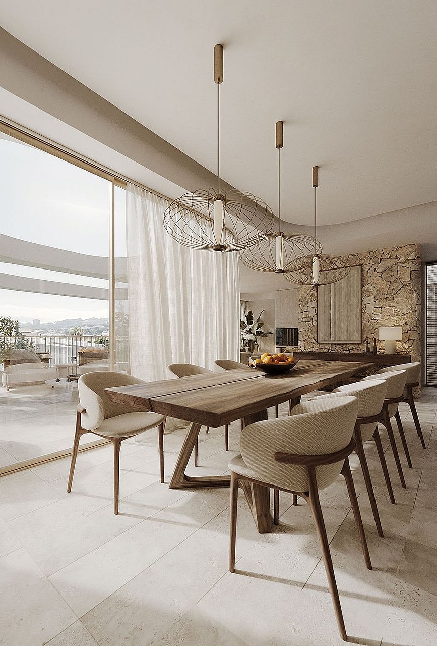 Dining area with long wooden table, cream upholstered chairs, and a natural stone feature wall, opening onto a balcony.