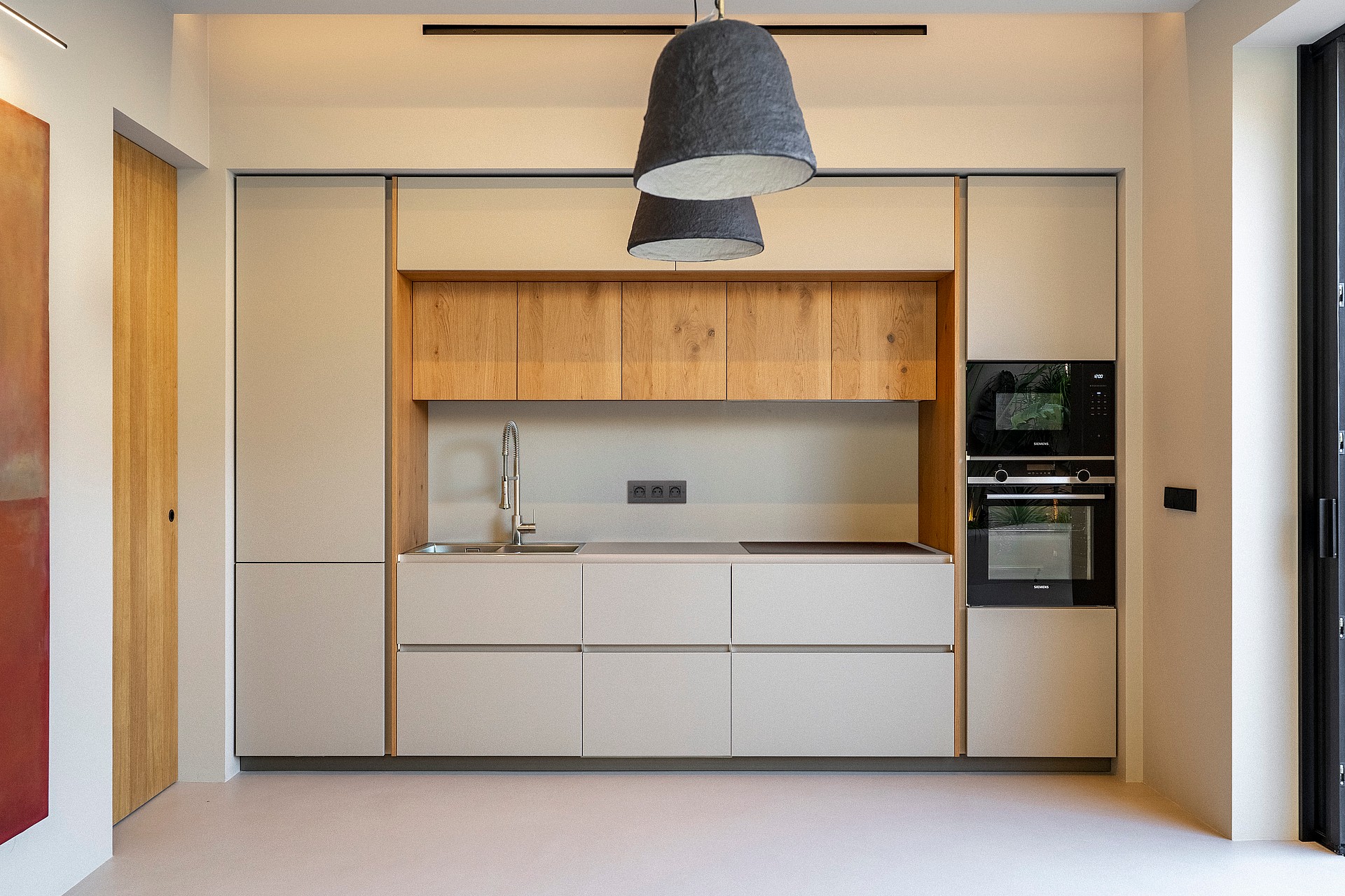 Modern kitchen featuring handleless cream cabinetry, oak upper shelving, integrated appliances, and grey pendant lights.