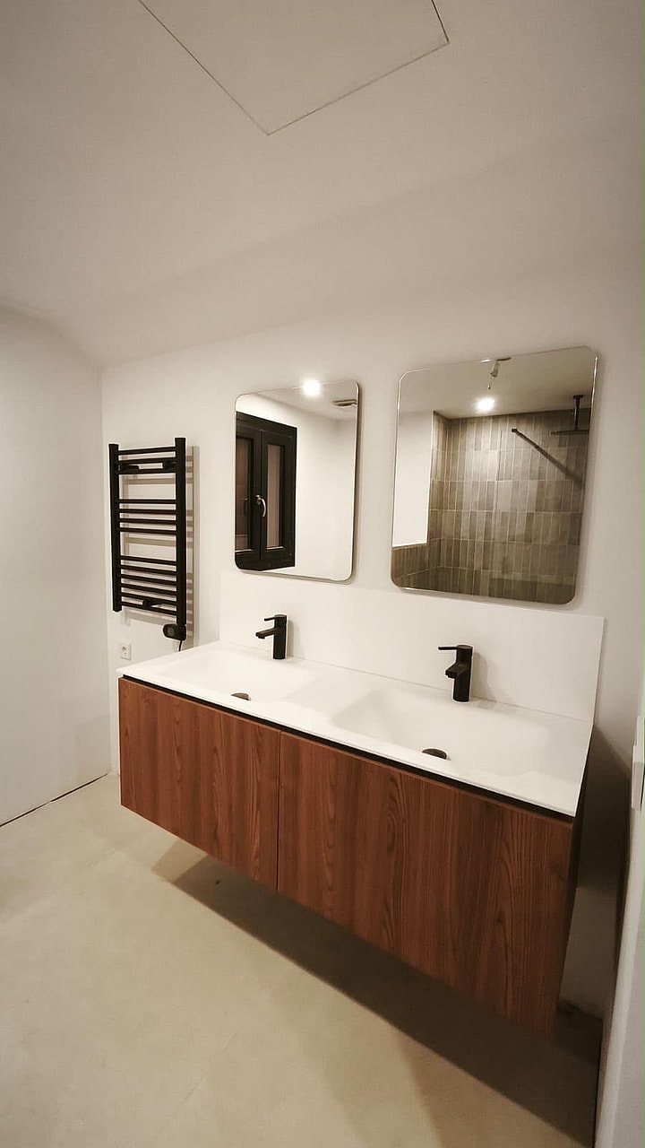 A modern bathroom featuring a wall-mounted wooden vanity with double sinks, two rectangular mirrors, and a black heated towel rail.