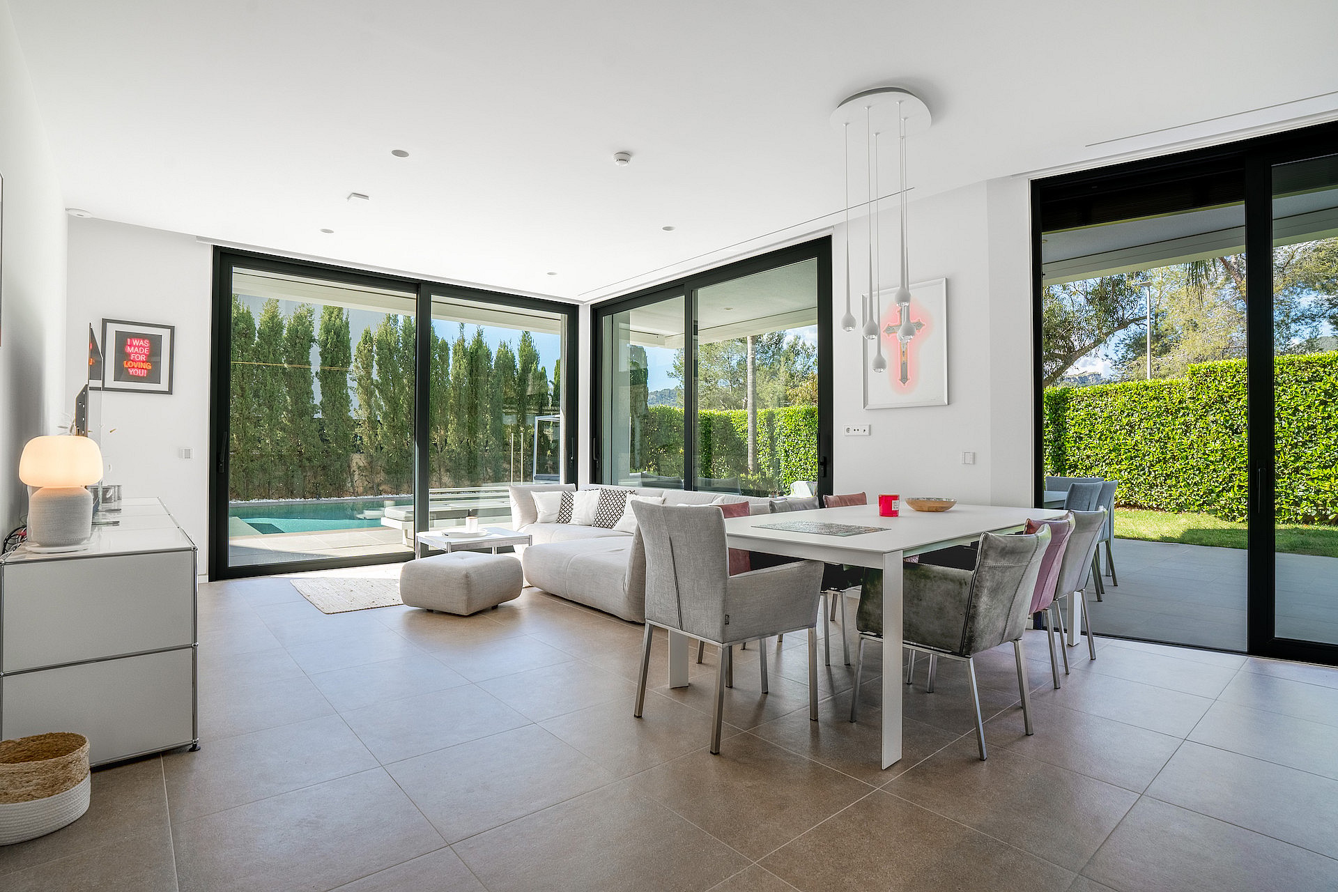 Open-plan living and dining room with corner sliding glass walls opening to the pool terrace and garden.