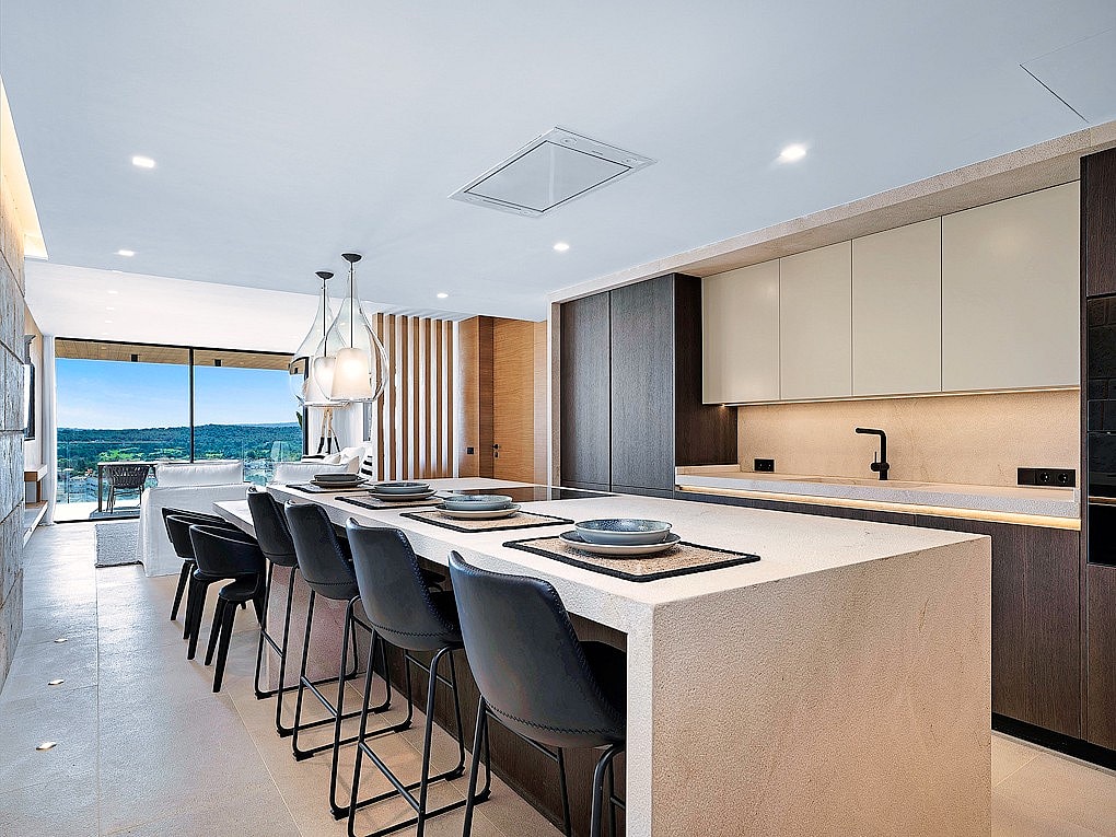 Modern kitchen with large white stone island, dark bar stools, and sliding glass doors opening to a mountain terrace.