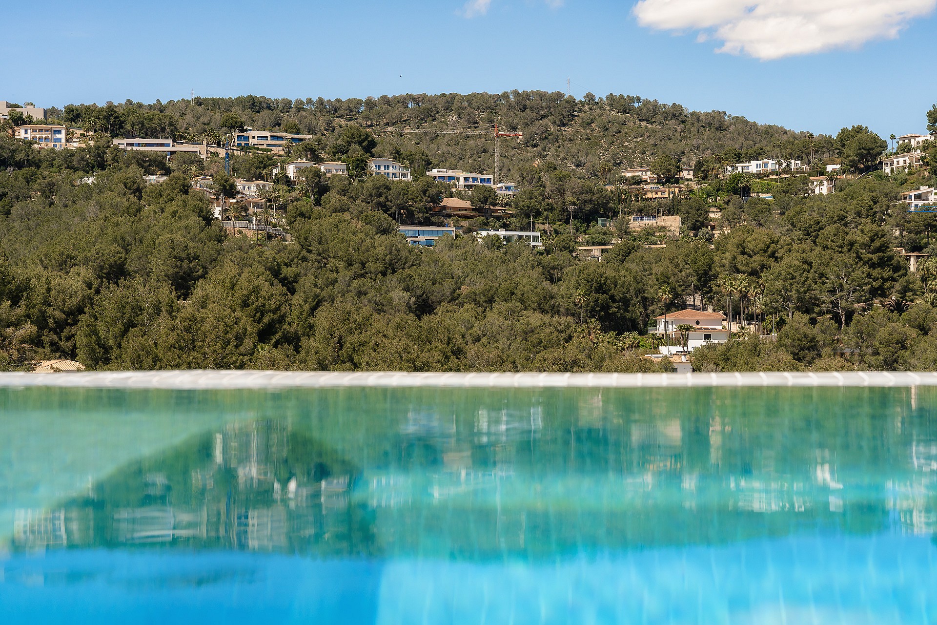 Close-up of an infinity pool edge reflecting the lush green hillside and villas of Son Vida under a clear sky.