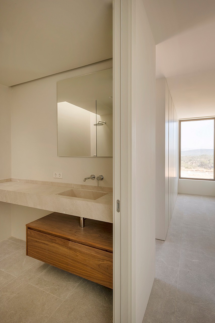 Contemporary bathroom featuring a floating wooden vanity, integrated stone sink, and a view through a sunlit hallway.