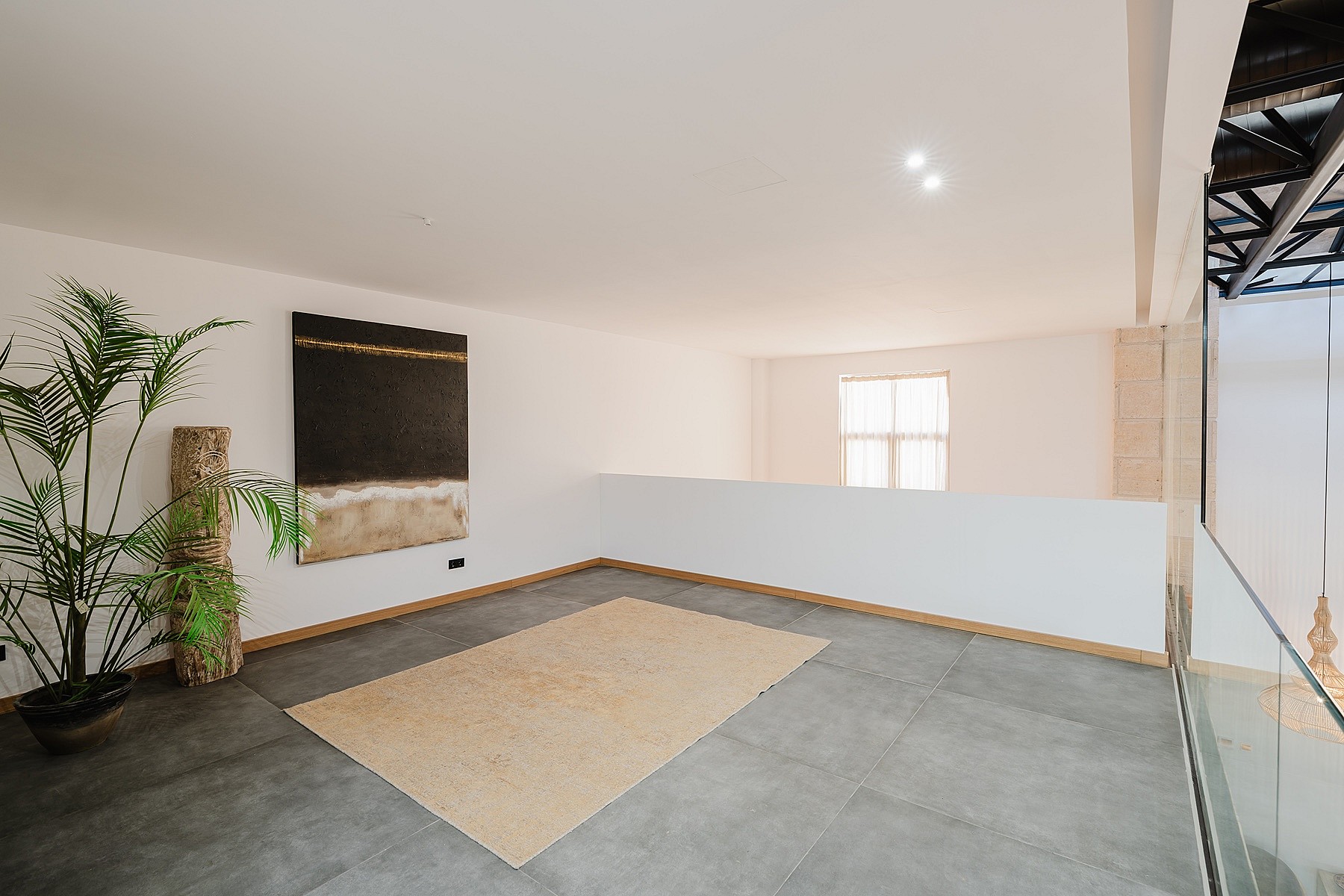 An open mezzanine landing with grey tiled flooring, white walls, and a large abstract painting, featuring a glass balustrade.