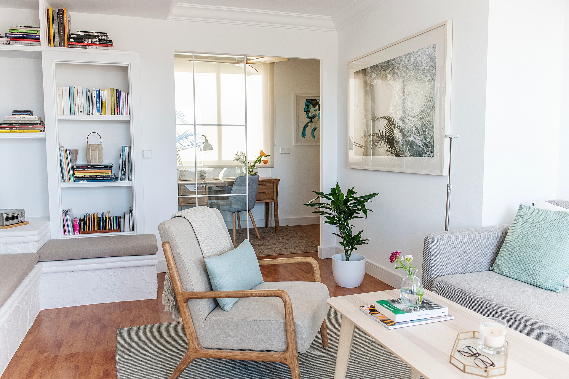 Living room with white walls, wooden floors, built-in bookshelf, and upholstered armchair, looking through a doorway.
