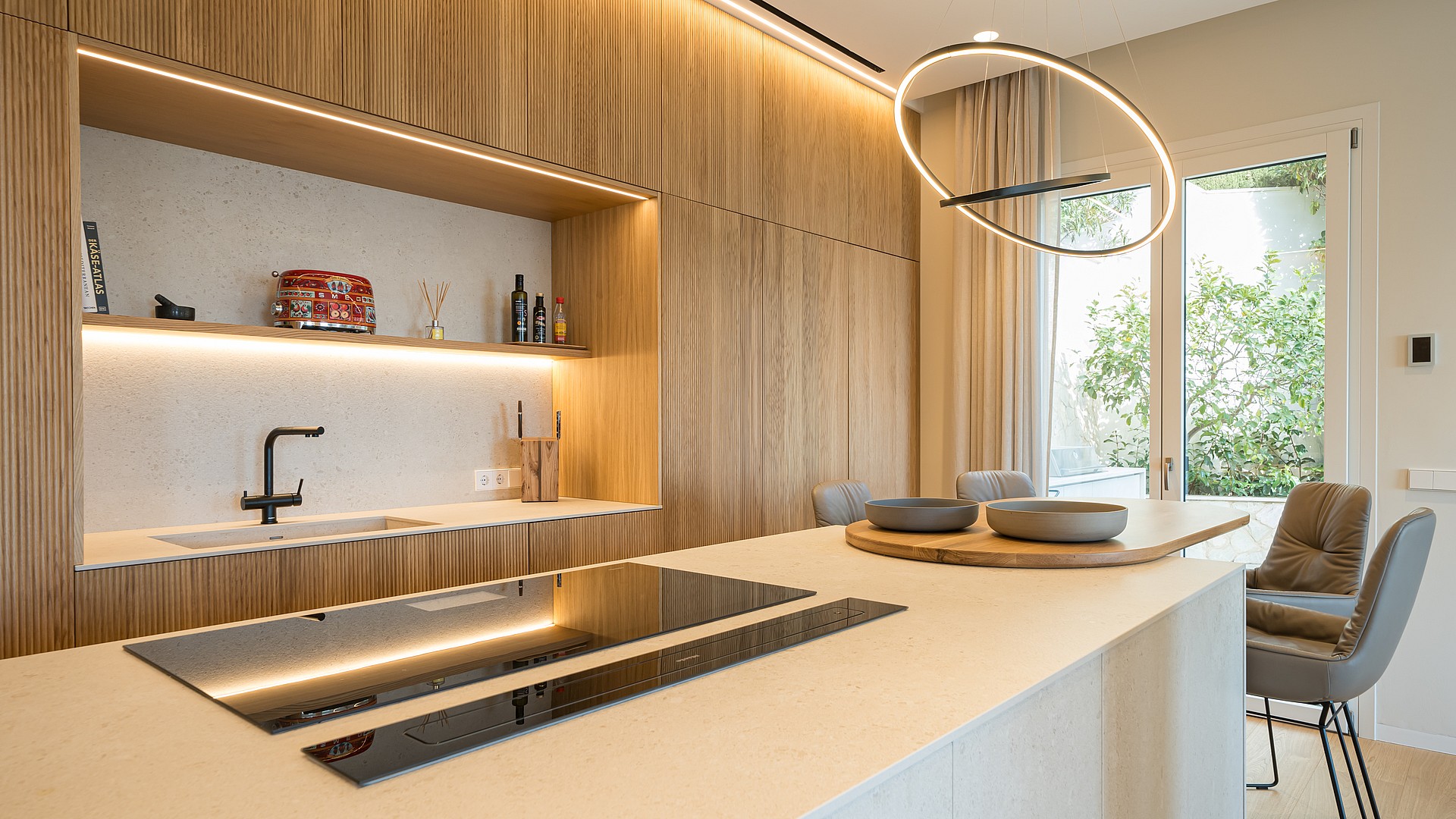 Modern kitchen featuring vertical oak slat cabinets, integrated lighting, a stone kitchen island, and a circular pendant light.