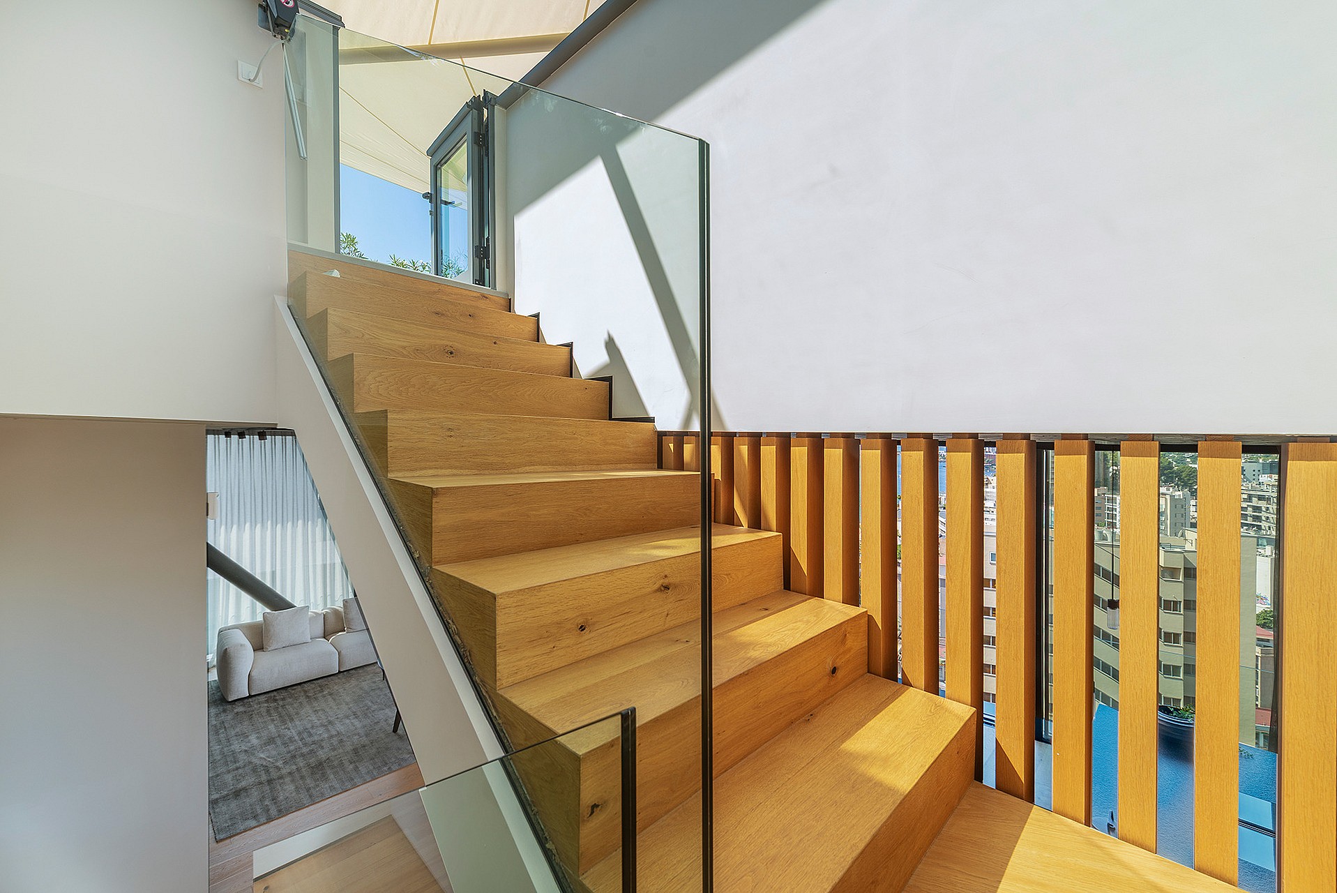 A modern interior staircase featuring solid oak treads and vertical timber slat railings, complemented by a transparent glass balustrade.