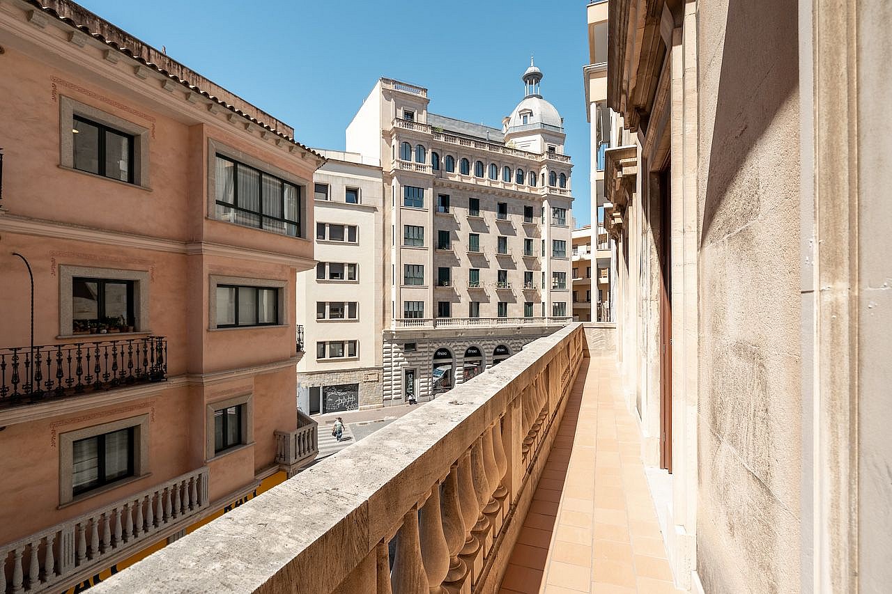 A stone terrace balcony with a classical balustrade overlooking a historic urban street with multi-story buildings in Palma.