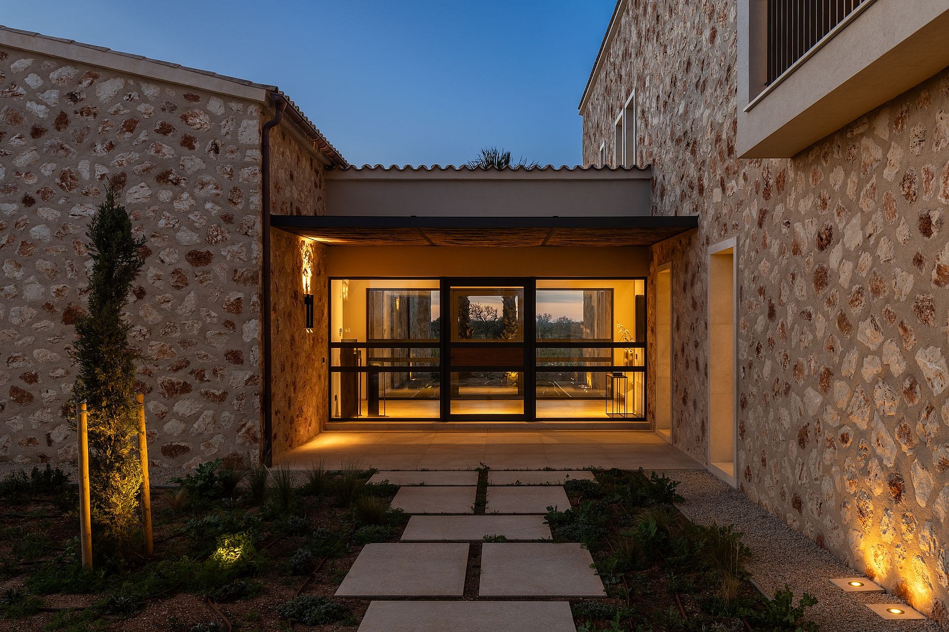 The entrance to a traditional stone finca at twilight with a stone pathway leading to a glass-paneled front door.