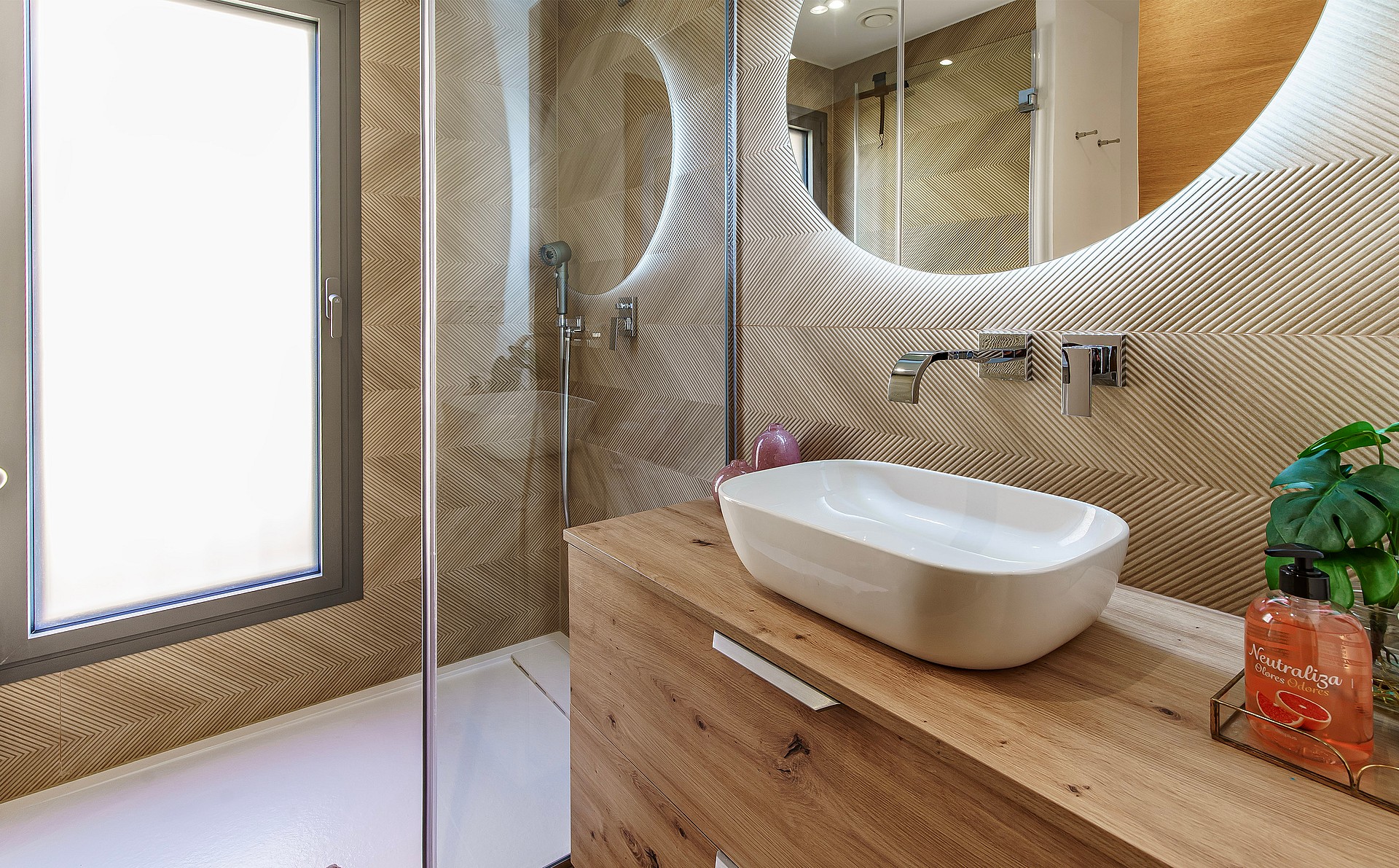 Modern bathroom featuring patterned beige wall tiles, a wooden vanity with a white vessel sink, and a glass-enclosed shower.