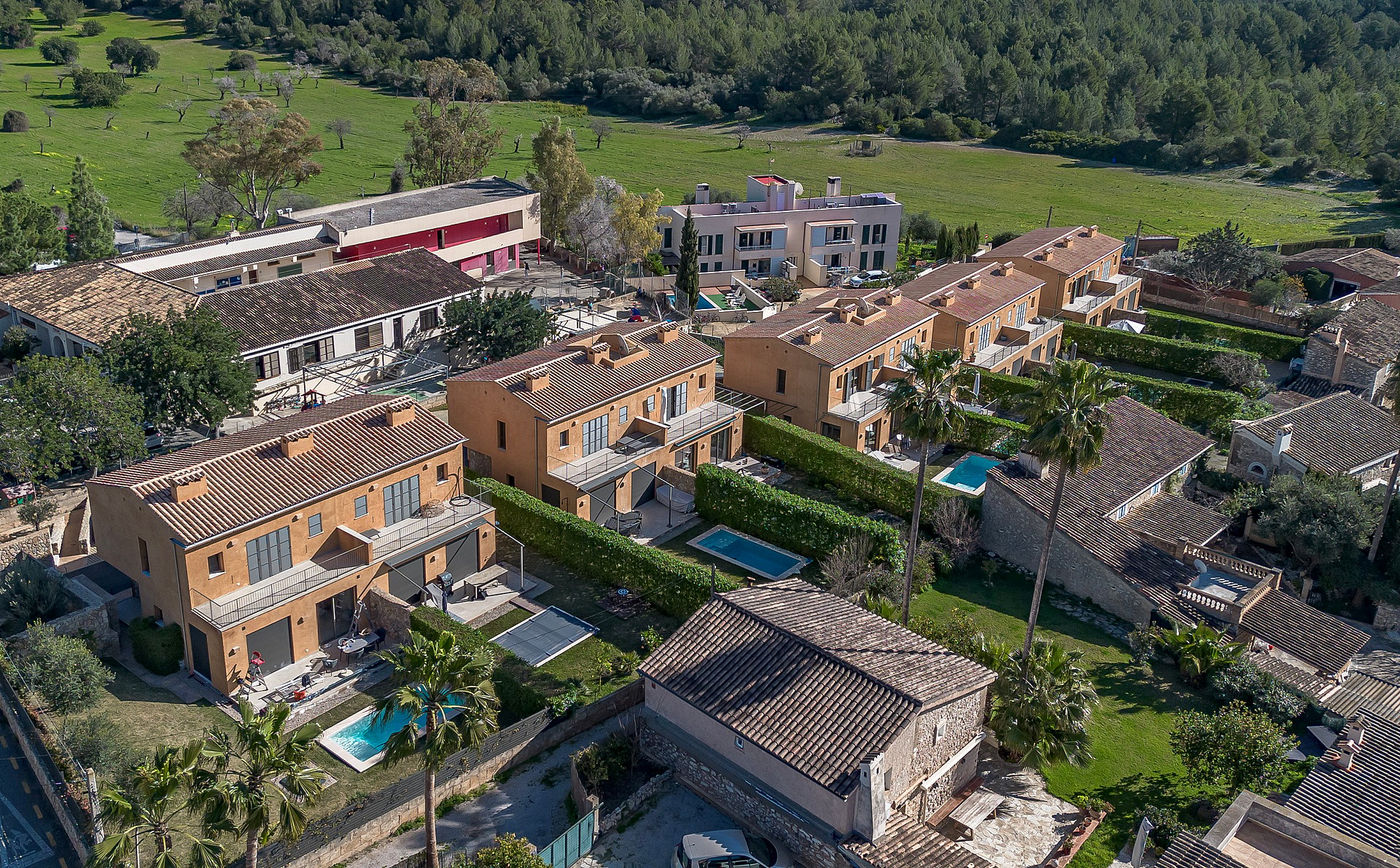 Aerial perspective of a cluster of terracotta-roofed townhouses with private pools and landscaped gardens in Es Capdella.