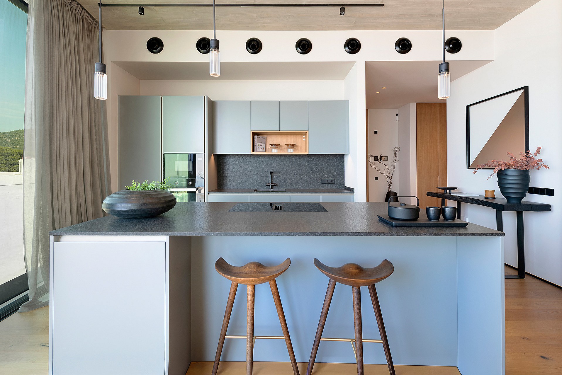 Contemporary kitchen featuring a grey island, dark stone countertops, wooden bar stools, and track lighting in a penthouse.