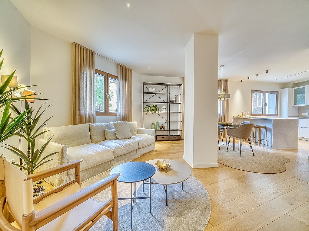Bright open-plan living room with a beige sofa, round coffee tables, wooden flooring, and adjacent dining and kitchen areas.