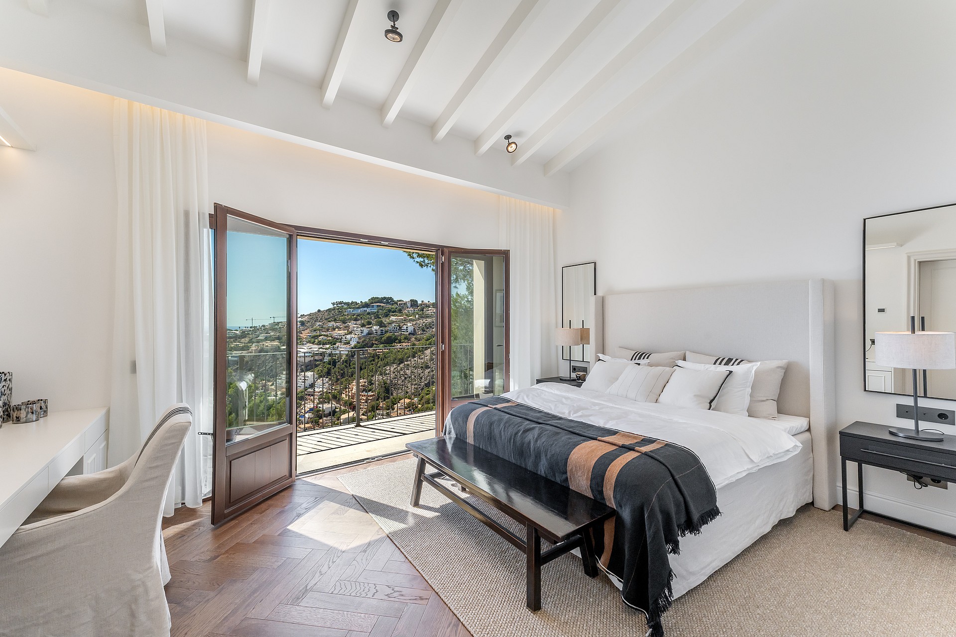 Bright bedroom with herringbone wood floors and open French doors leading to a terrace with sweeping valley views.