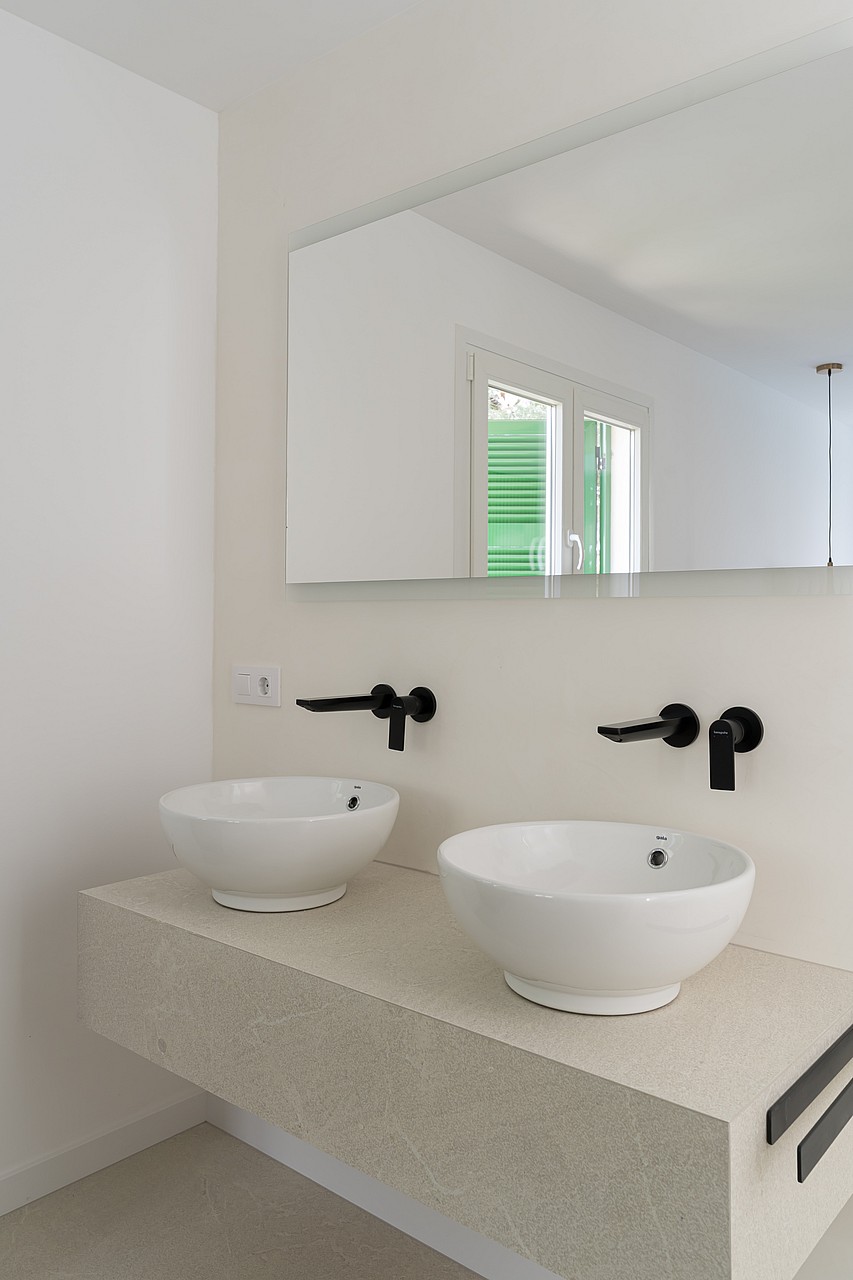 Dual white ceramic vessel sinks on a floating stone vanity with matte black wall-mounted faucets and integrated side rails.