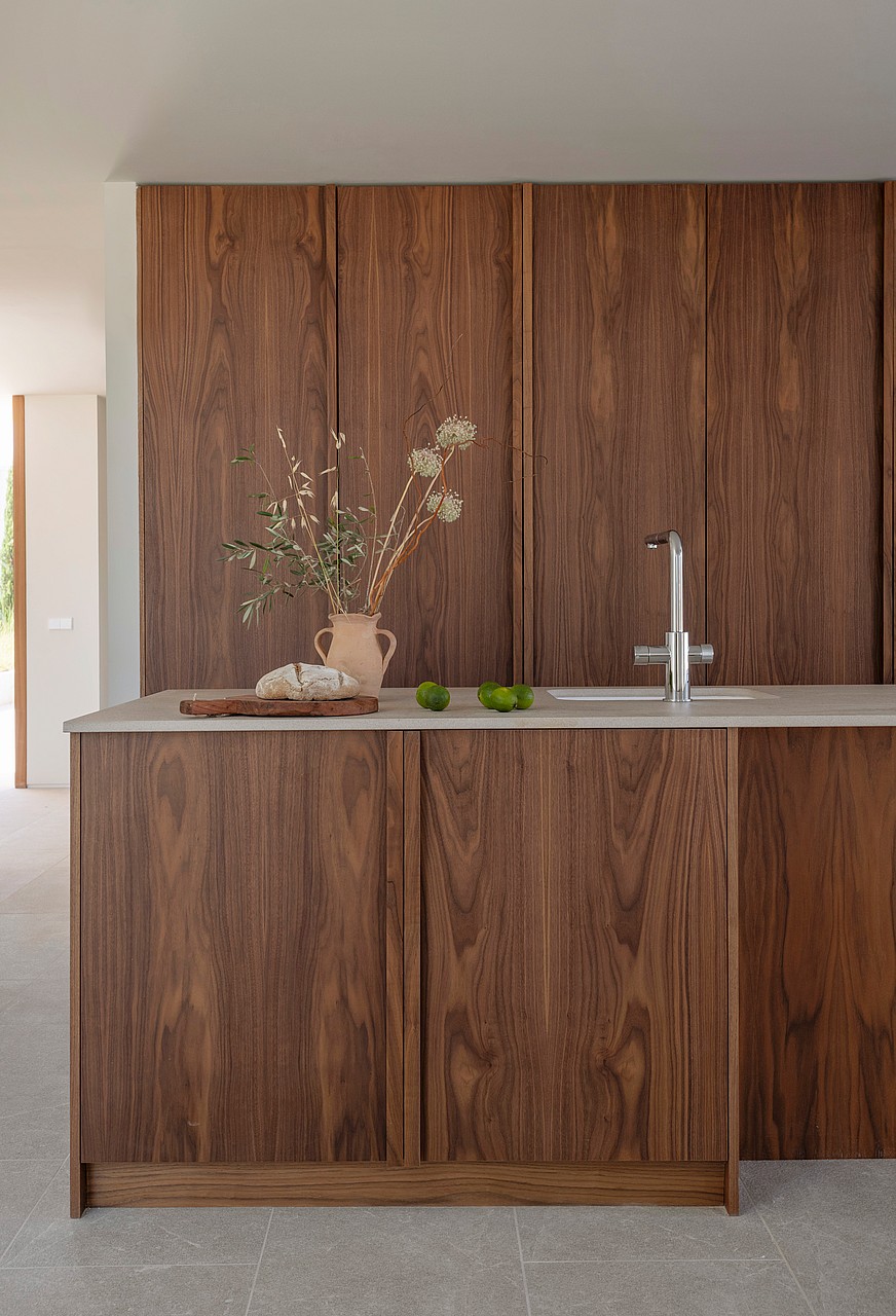 Close-up of a kitchen featuring vertical grain walnut cabinets, a light gray stone countertop, and a modern chrome faucet.