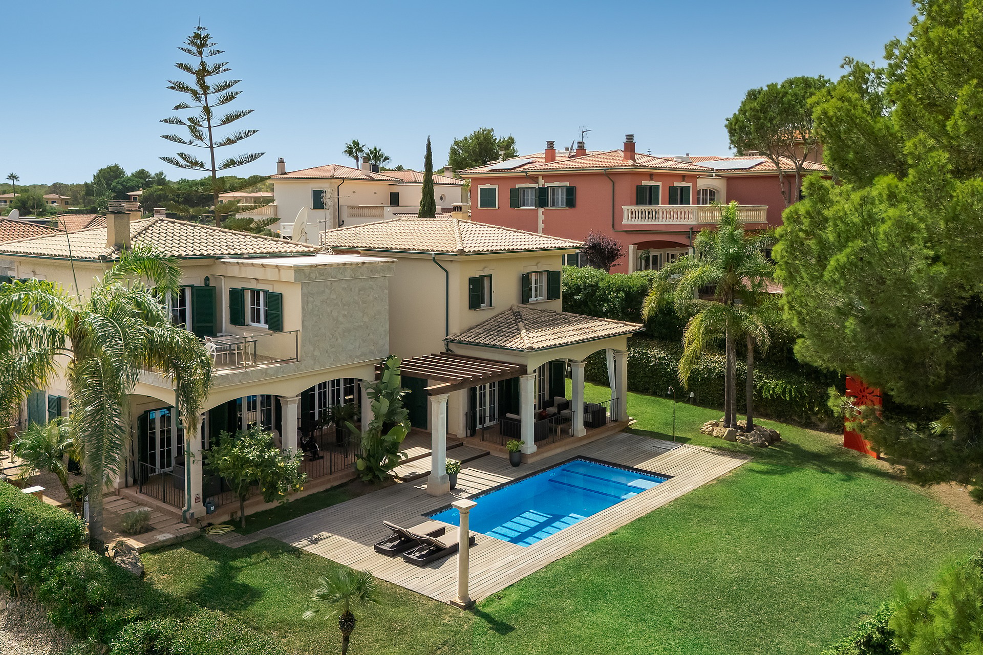 A two-story villa with Mediterranean architecture, a tiled roof, green louvered shutters, and a swimming pool in the garden.