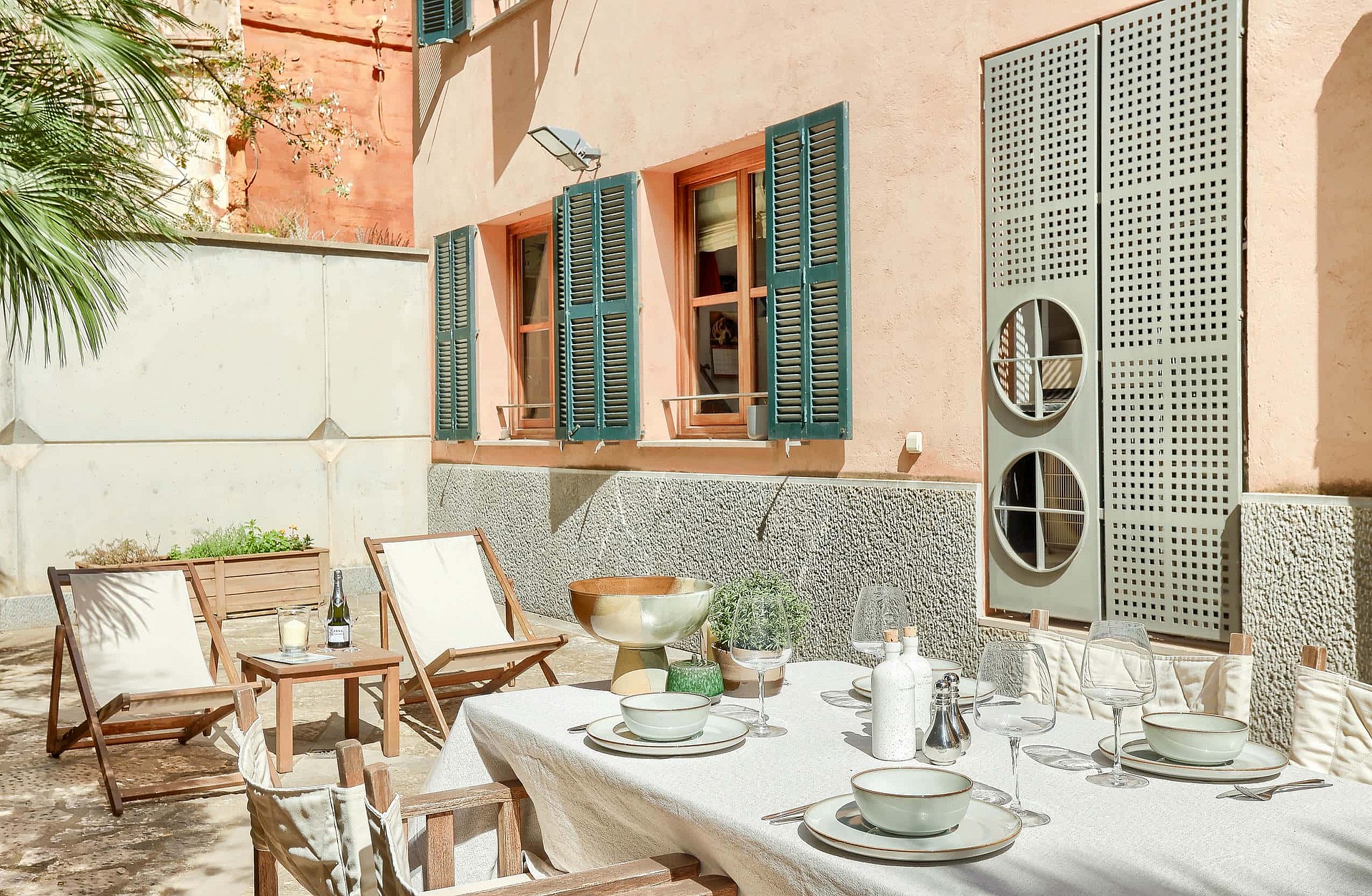 A private outdoor terrace in the Old Town with a dining table, folding wooden chairs, patterned stone wall, and green shutters.