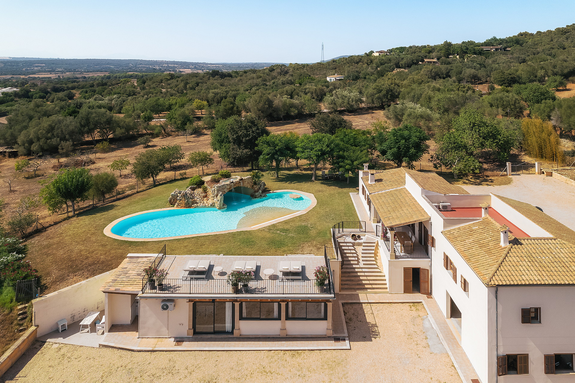 Vista aérea de finca en Manacor con piscina curva, tejados de teja y paisaje montañoso.