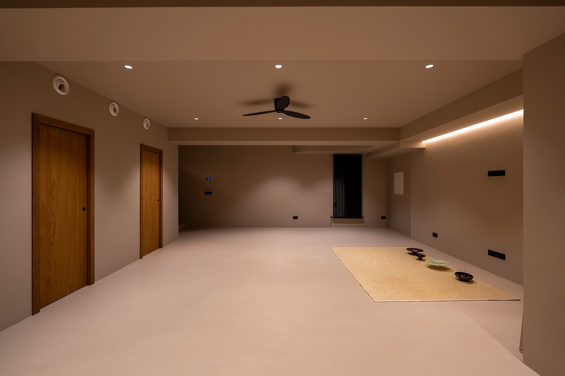 Minimalist multi-purpose room with grey walls, wooden doors, and integrated warm LED lighting.