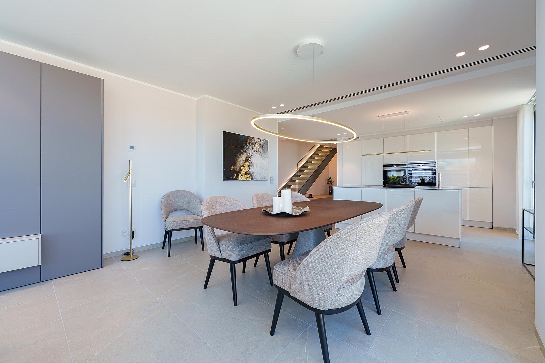Comedor con mesa ovalada de madera y seis sillas, junto a una cocina blanca minimalista con iluminación empotrada.