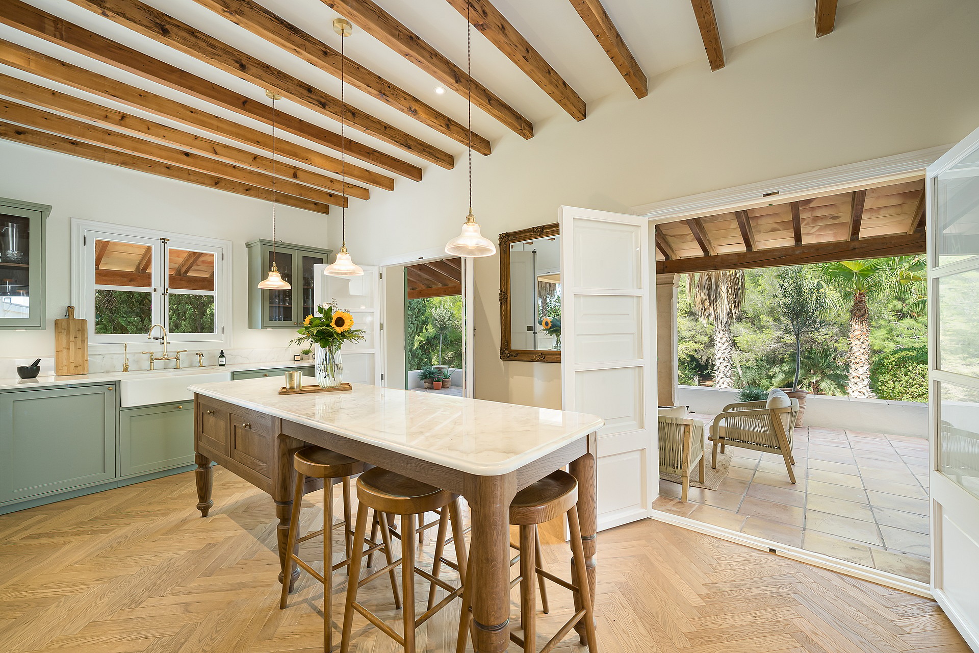 Traditional kitchen featuring sage green cabinetry, exposed timber ceiling beams, and a marble-topped central island.