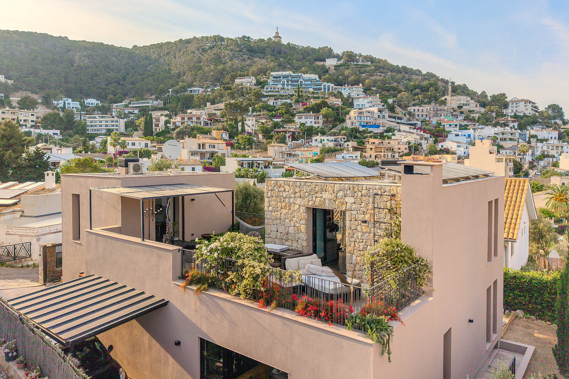An elevated view of a contemporary villa with stone facade and rooftop terrace overlooking a hillside residential area.