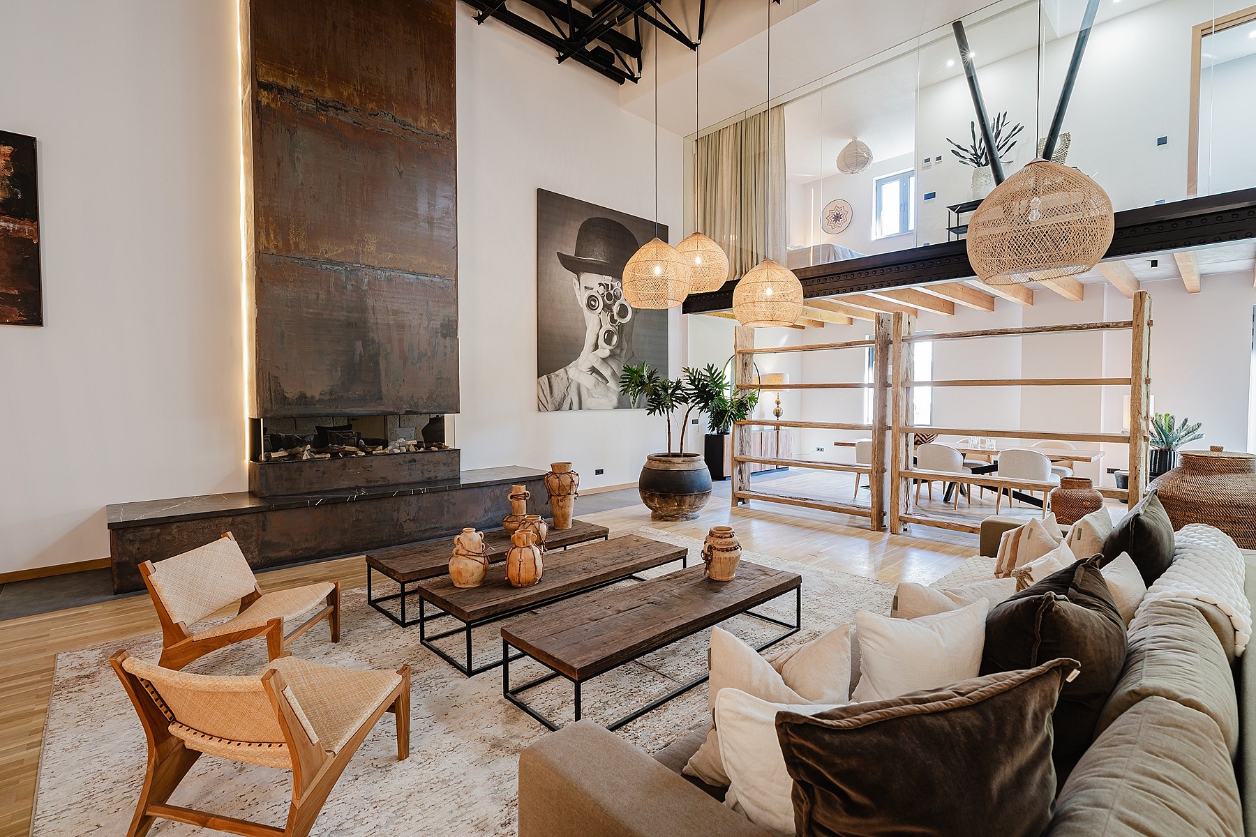Modern open-plan living room with high ceilings, tall metal fireplace, wooden shelving, and warm pendant lighting.