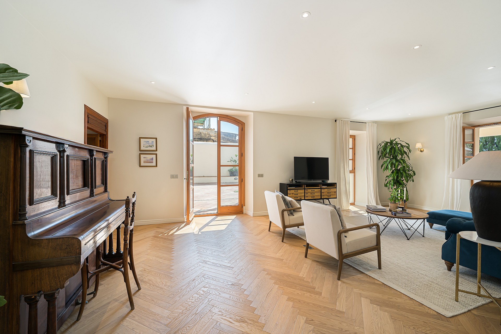 Bright living room featuring light oak herringbone parquet flooring, a classic upright piano, and arched patio doors.