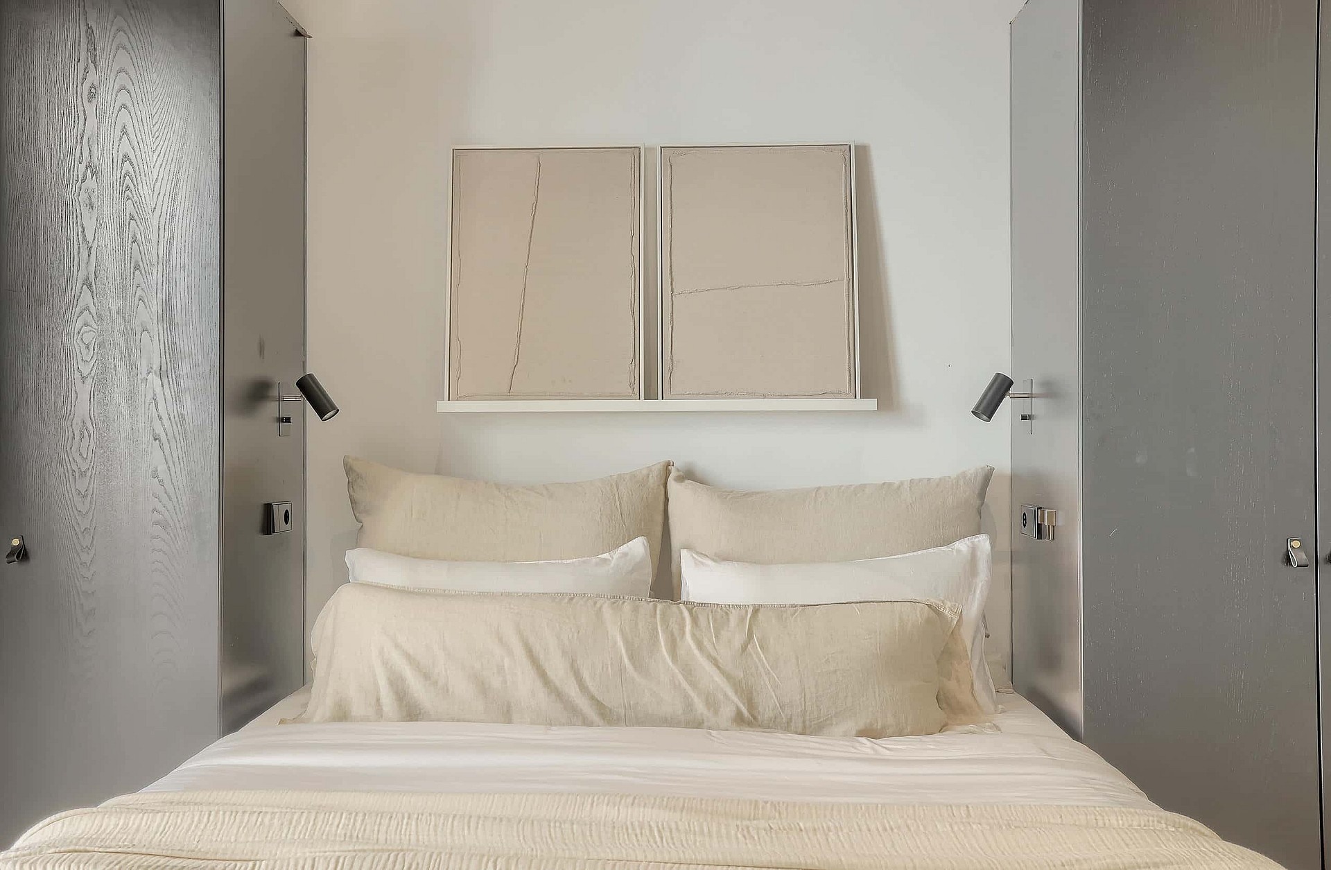 A symmetrical bedroom setup featuring a bed centered between two tall, grey, matte-finish cabinets with integrated wall lighting.
