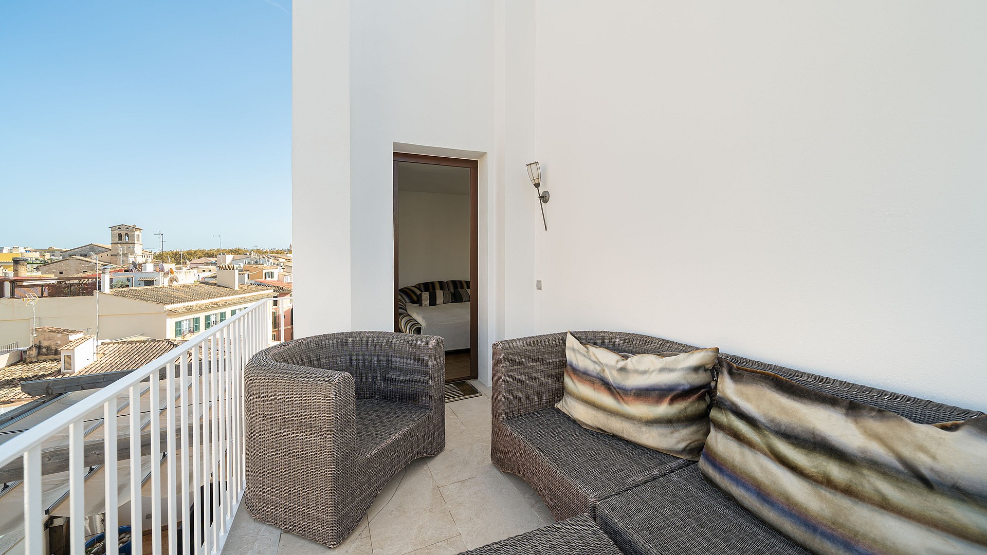 Rooftop terrace with grey wicker lounge furniture and white railings overlooking the historic city of Palma.