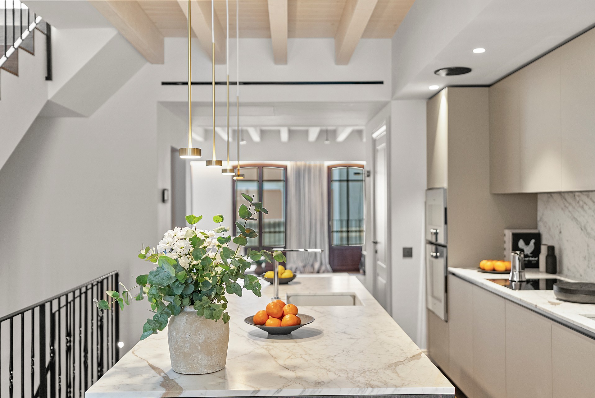 A white marble kitchen island featuring brass pendant lights, floral arrangements, and exposed light wood ceiling beams.